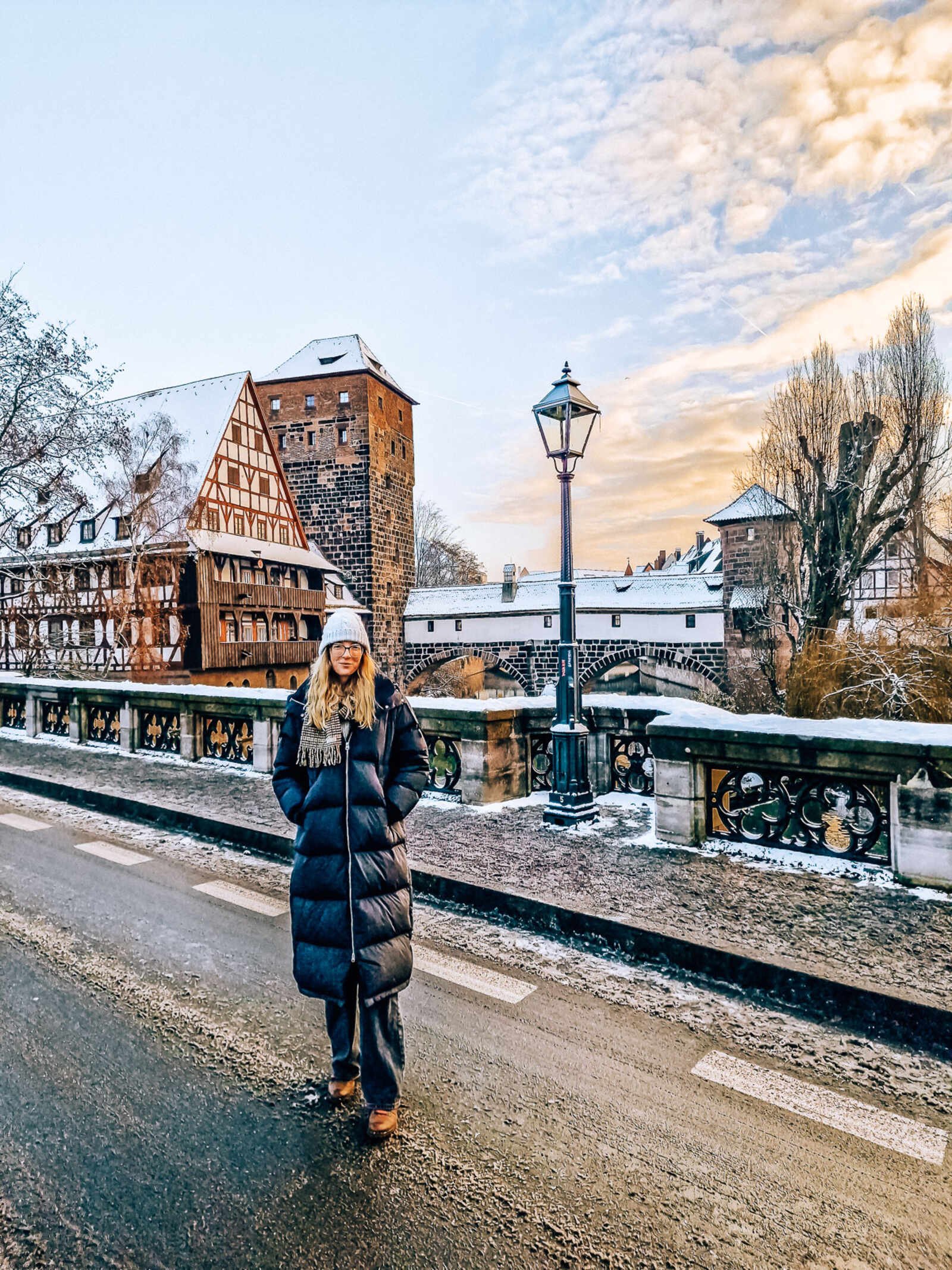girl in a big duffel coat on a snow covered bridge overlooking nuremberg old town buildings