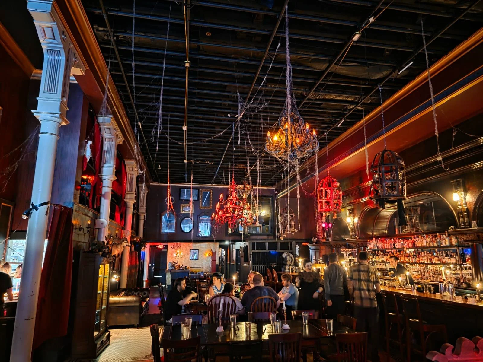 Inside a dark goth bar with red chandliers and spider webs hanging from the ceiling