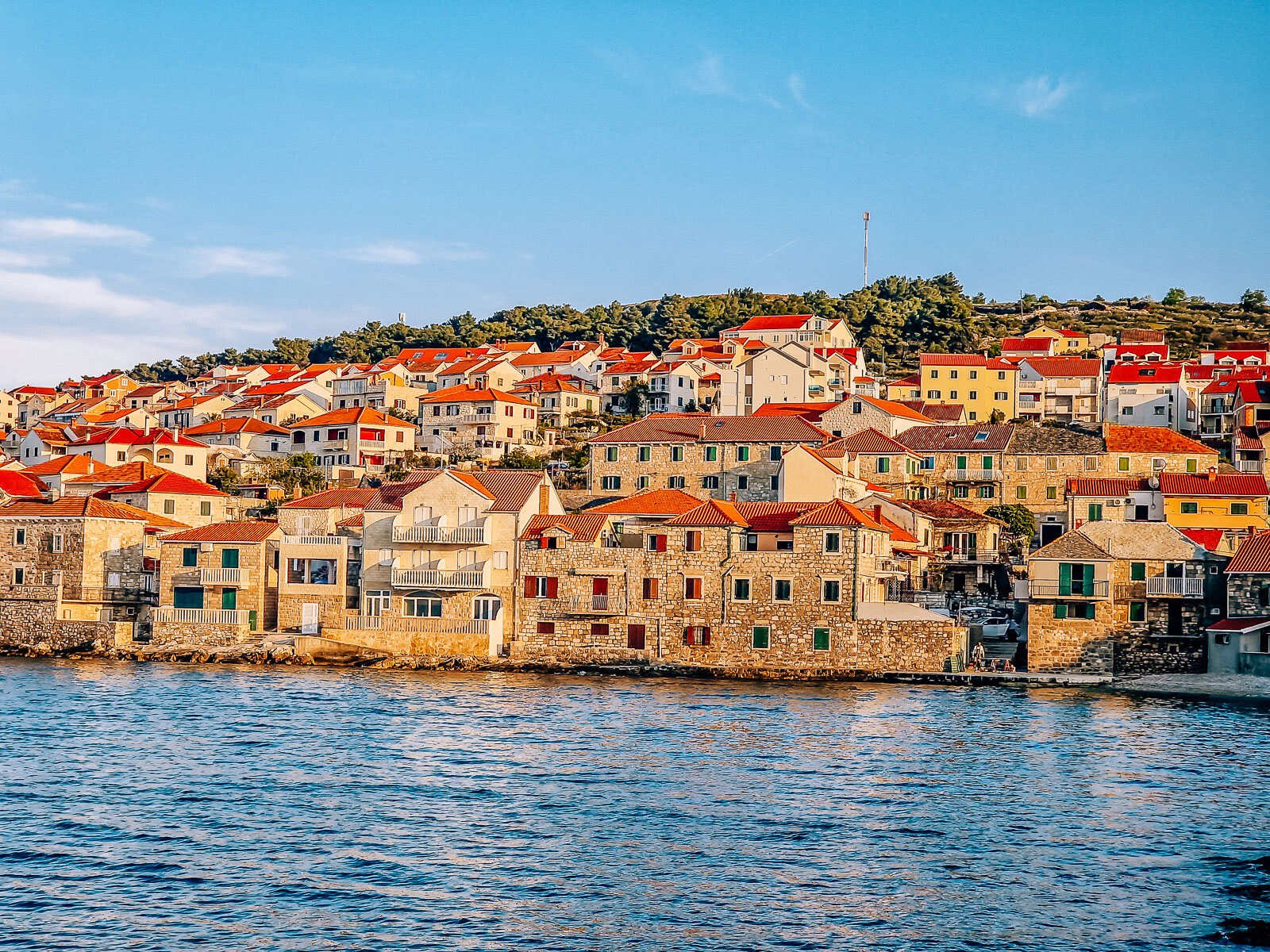 Croatian stone houses with orange roofs on the edge of the sea at sunset