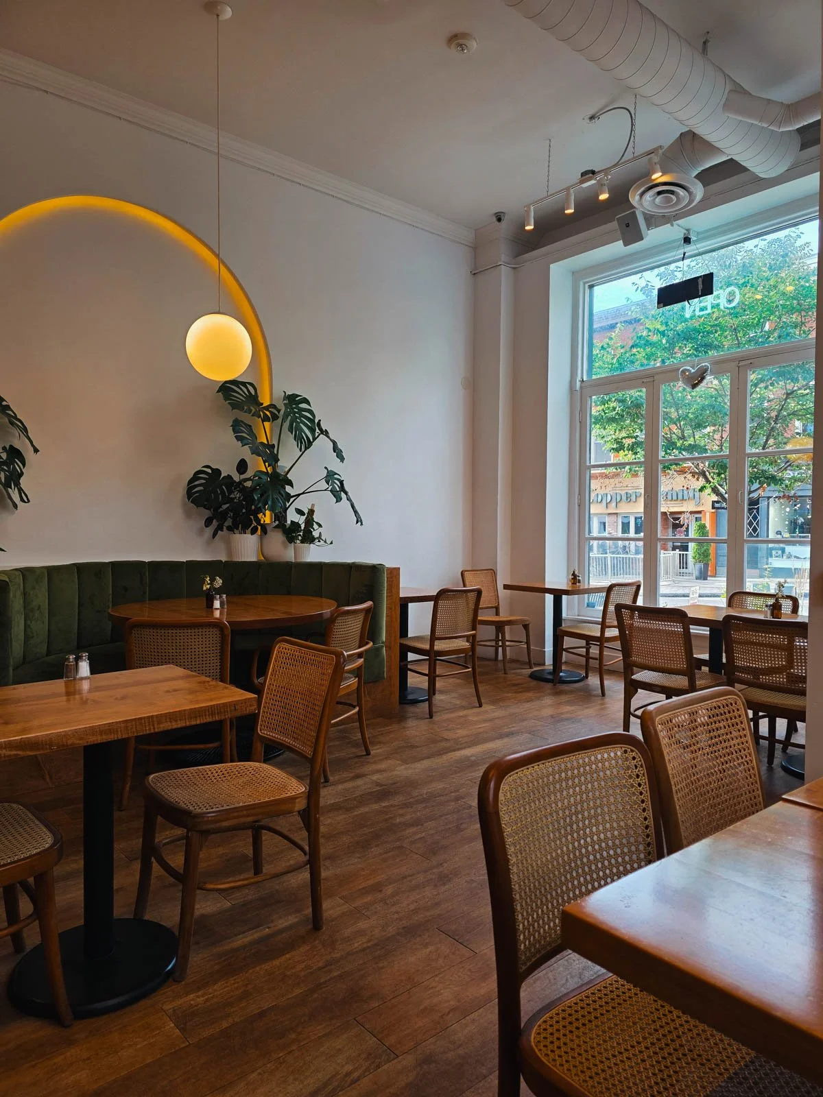 The interior of a café with wooden tables, wicker chairs, a green booth, wood floors, and large windows