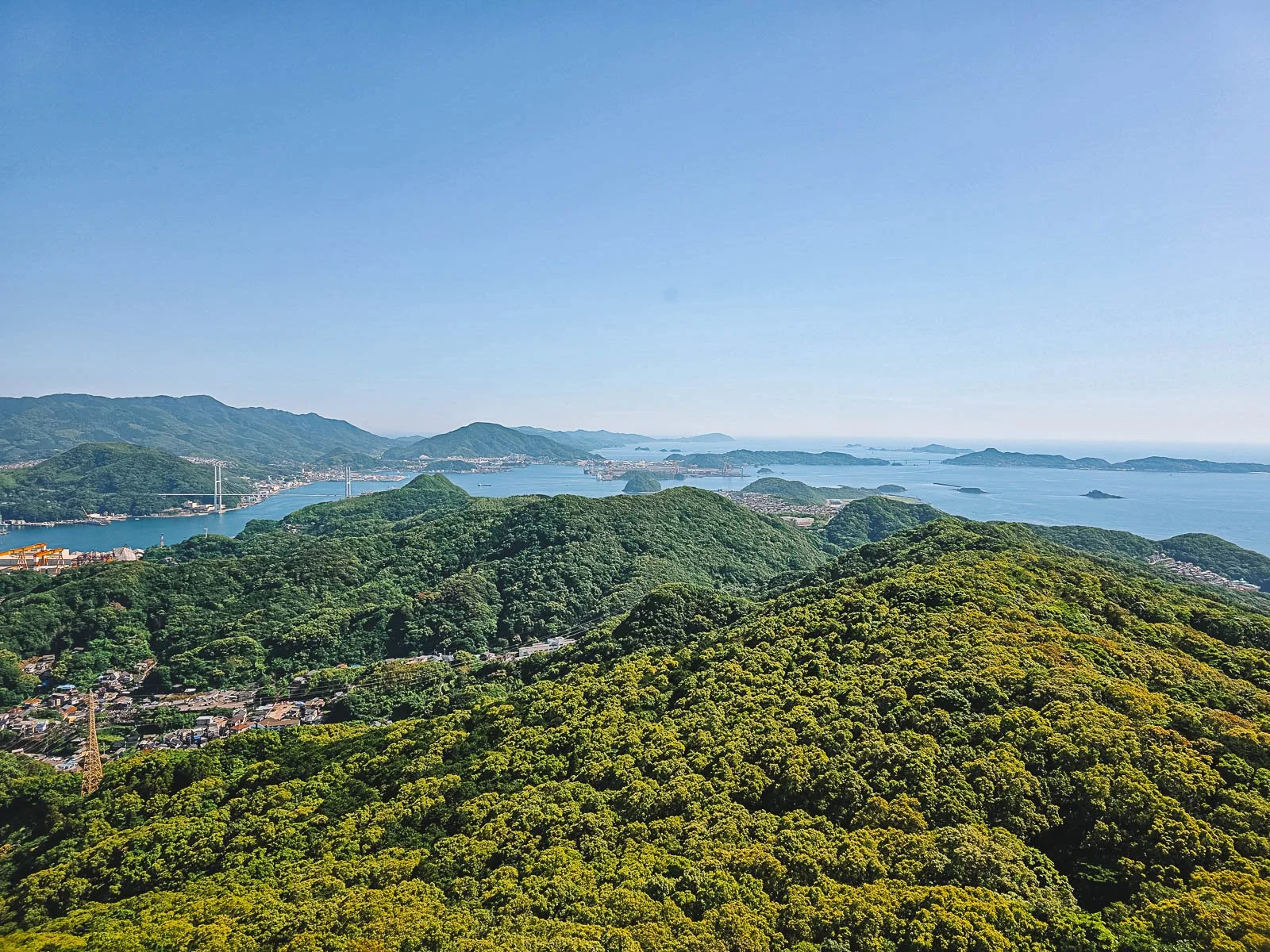 A mountain top view of many green hills with islands and blue water in the far distance around Nagasaki in Kyushu Japan