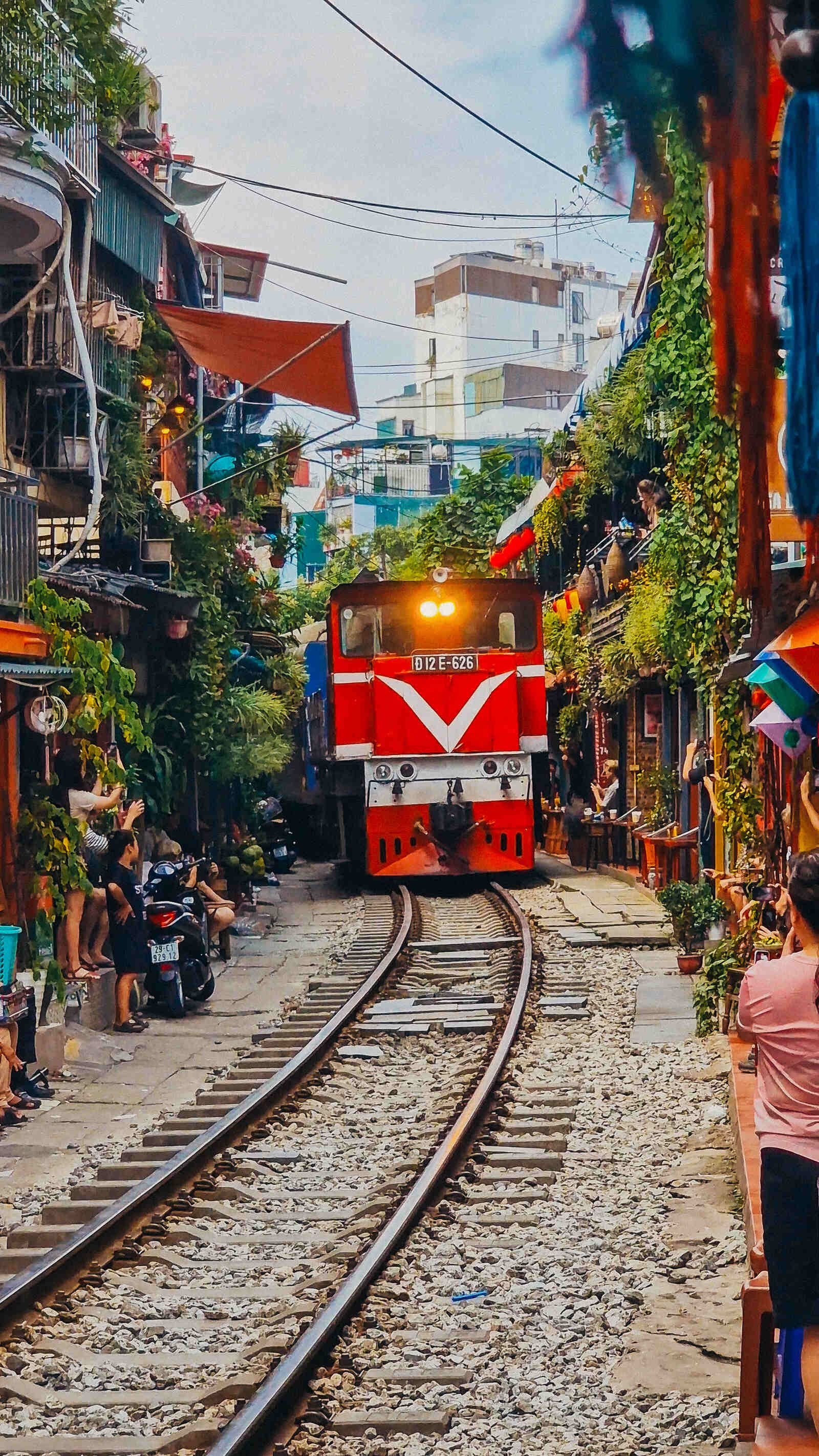 a train coming down a narrow street lined with houses and people at Hanoi train street in Vietnam