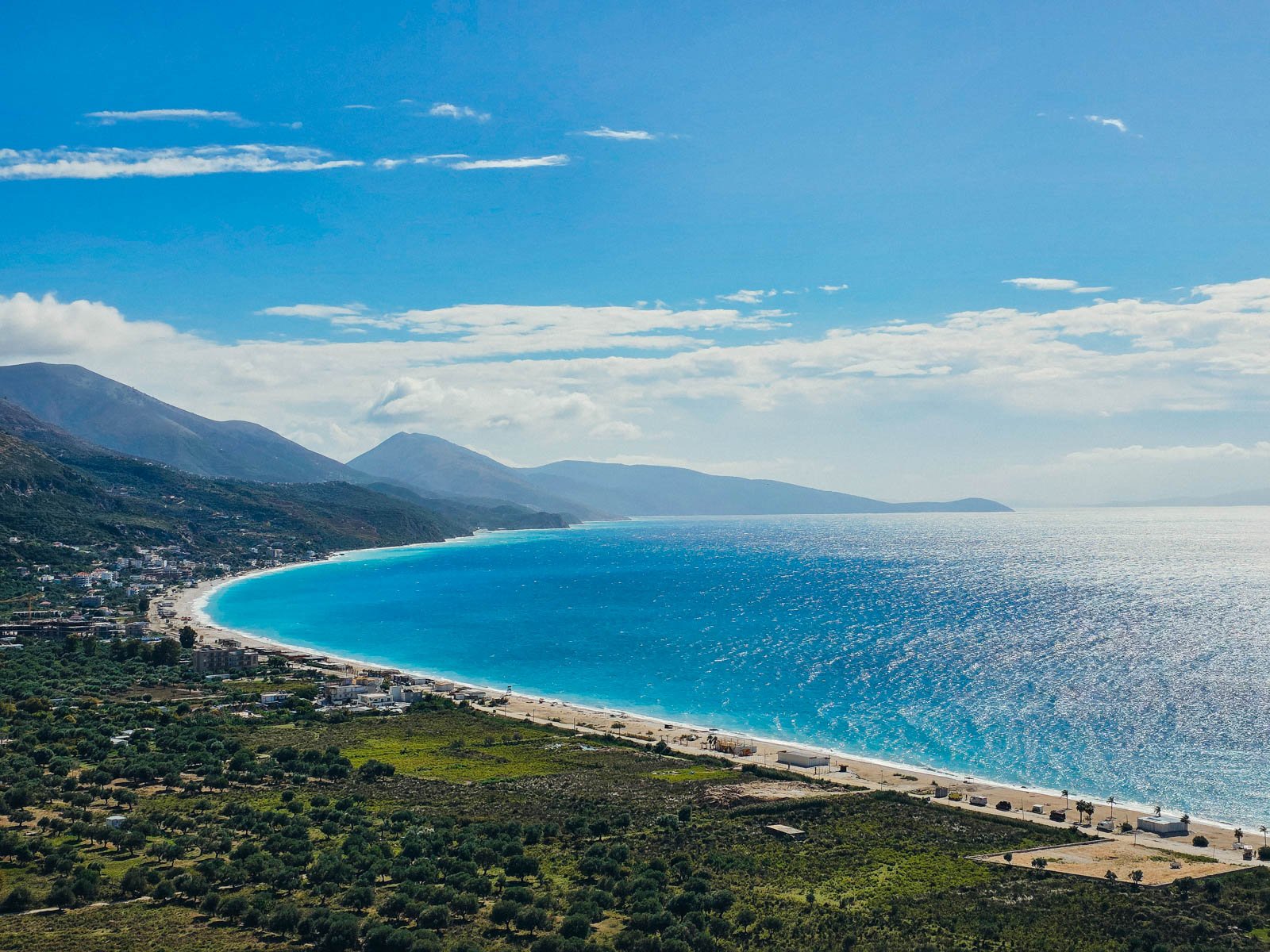 A curved clear blue watered coastline along the Albanian Riviera with white beaches and green hills