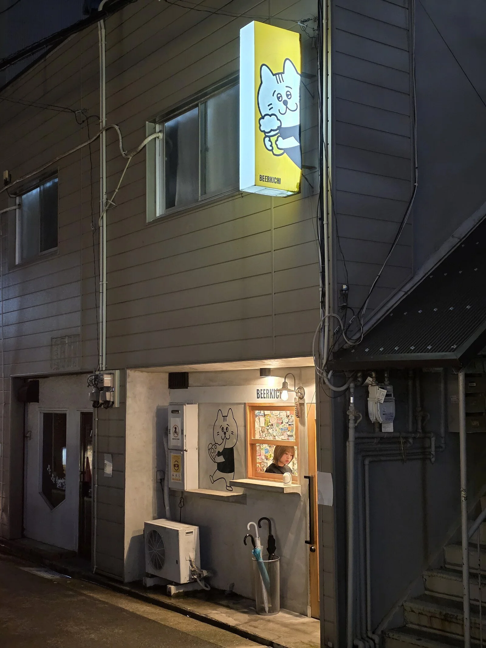outside a cute, small shop which is a beer stall with a small serving hatch and warmly lit. The logo is a cartoon cat