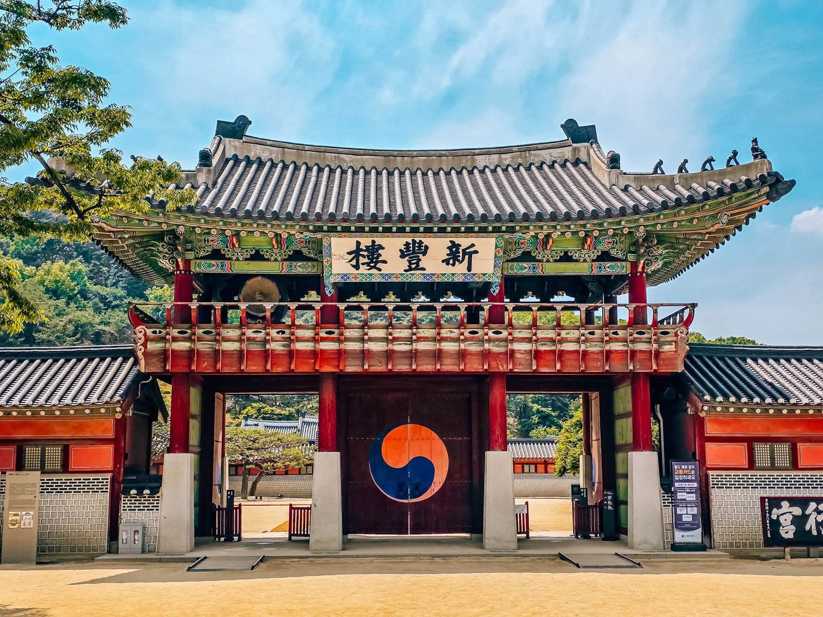 A large fortress gate with an ornate roof and large pained wooden gate door