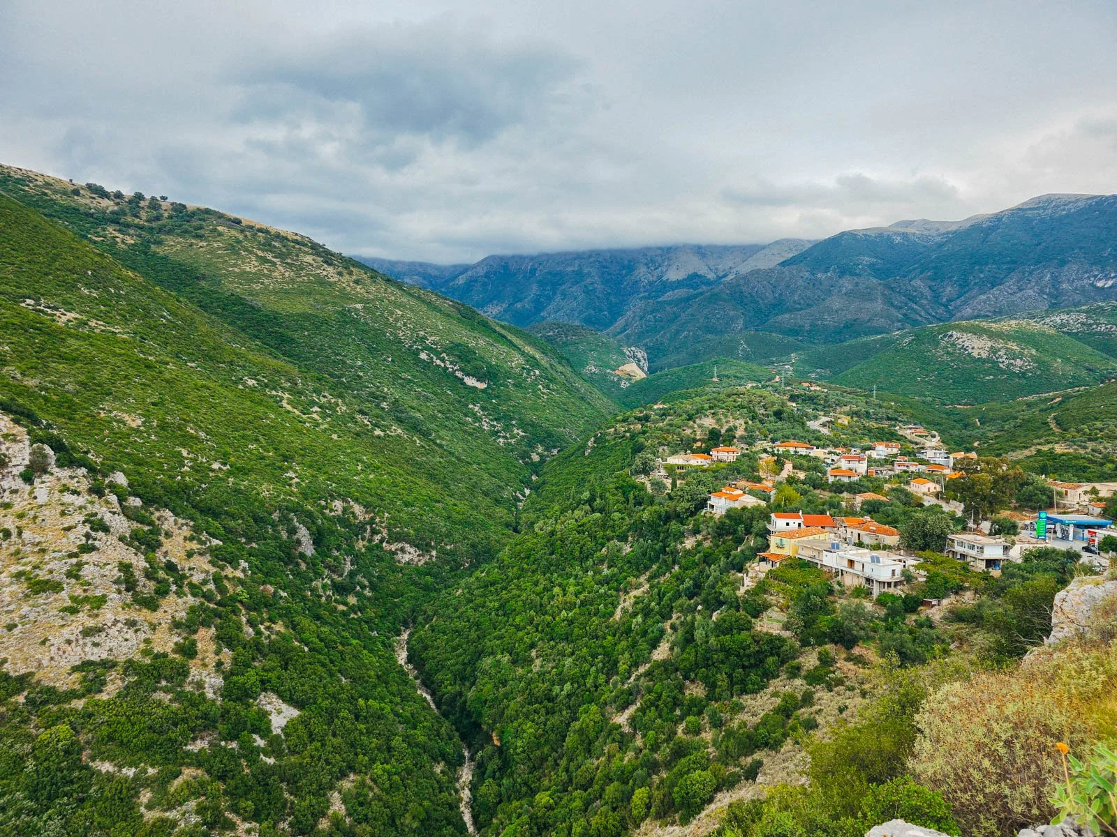 A long green ravine with green hills and many houses with orange roofs along the hills