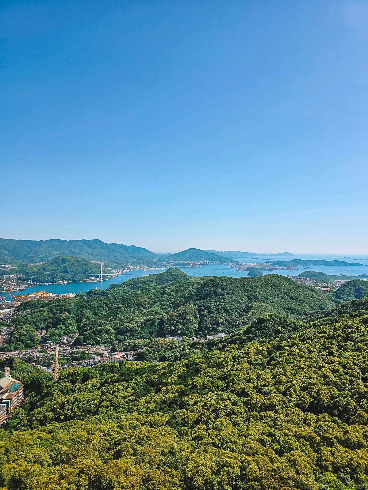 Viewing looking across lush tree covered hills and islands in a bay with blue water and blue skies in Nagasaki city, Kyushu Japan