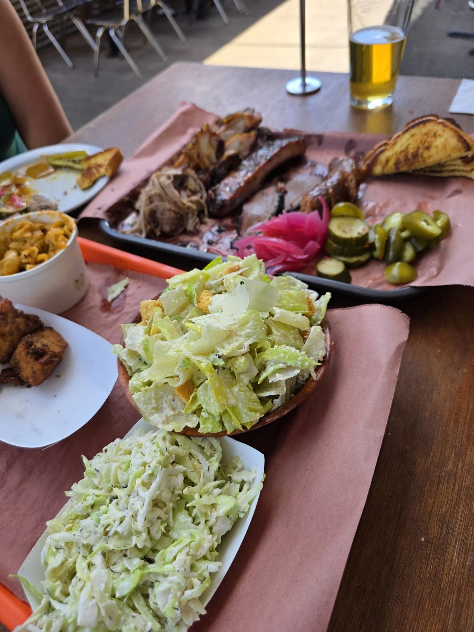 A plate of barbecue with lots of meat and sides on red paper on a table