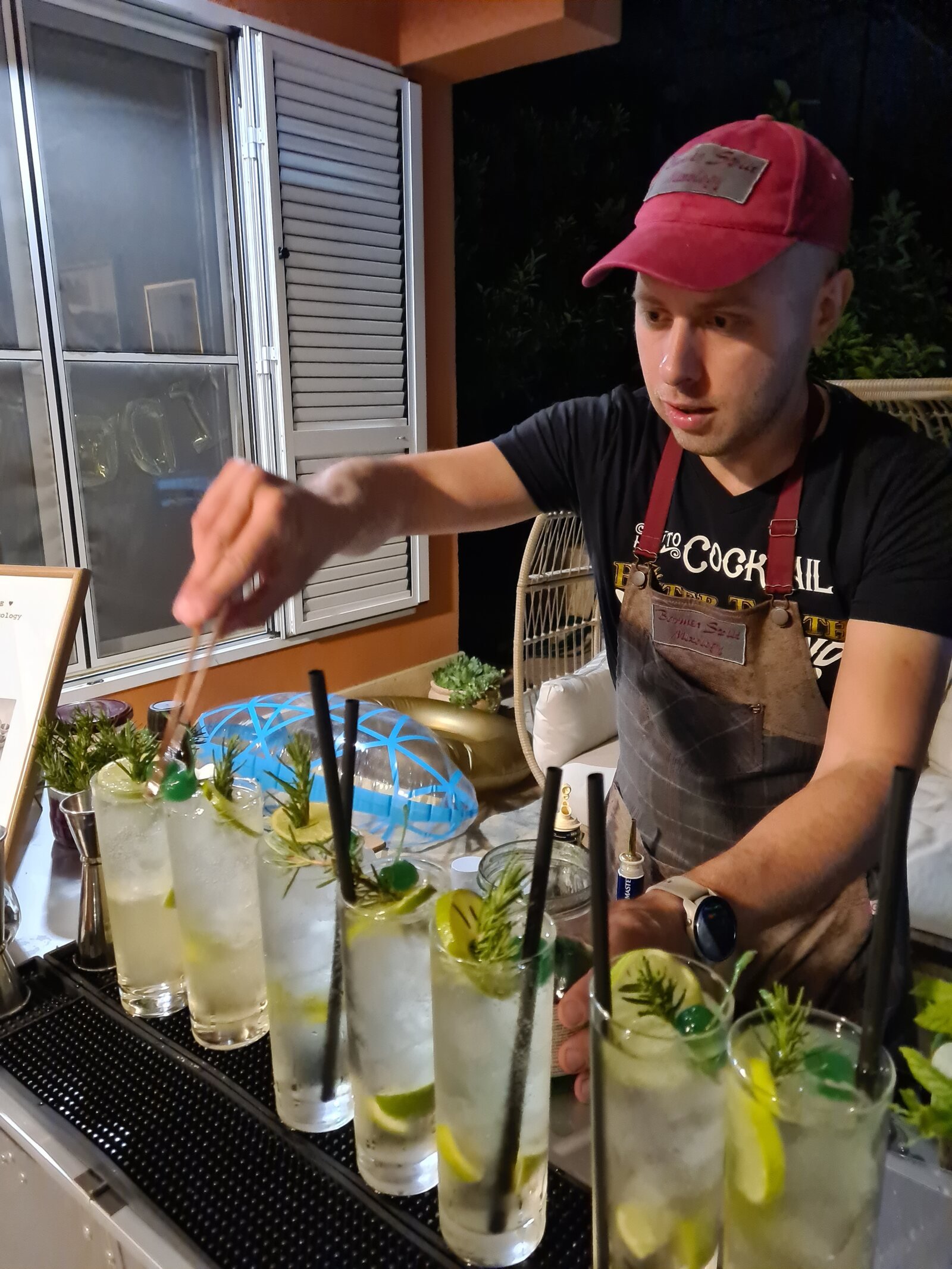 a man adding garnish to the last drink in a line of 7 drinks on a bar
