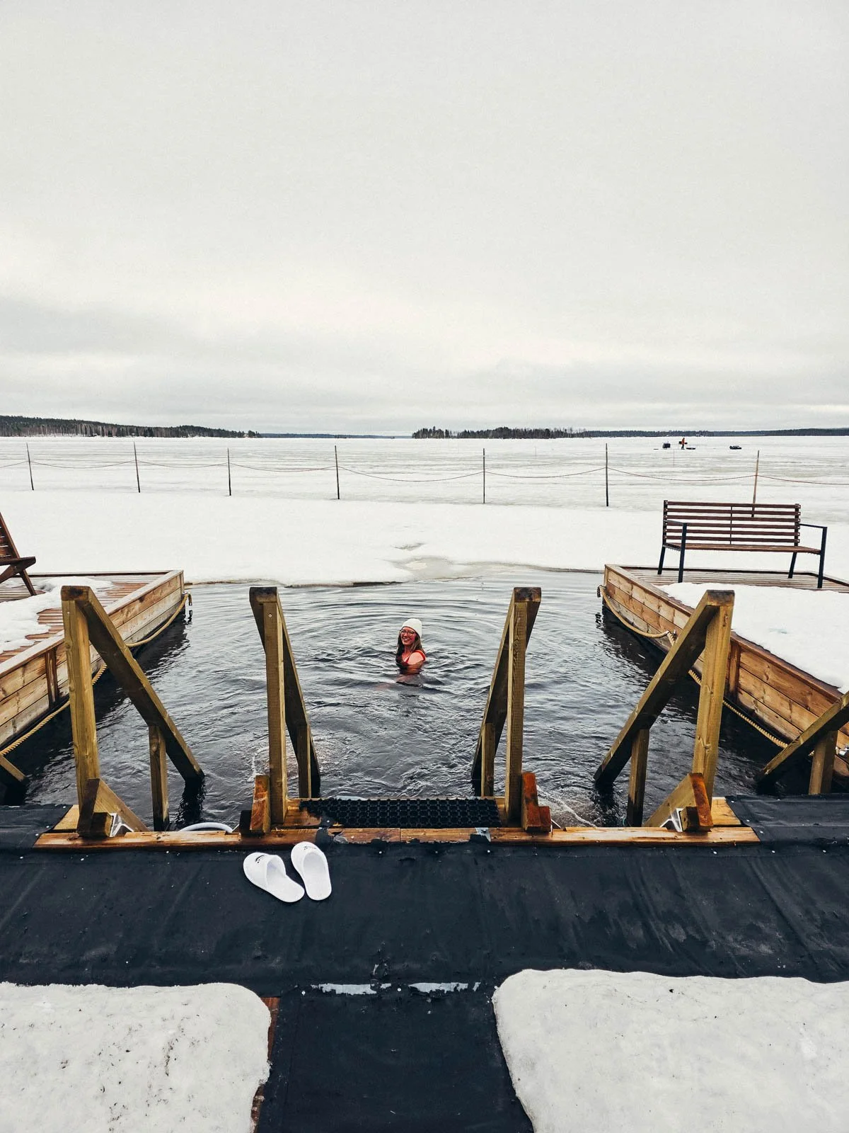 Helena swimming in a frozen lake cold plunge which has a wooden frame and stairs leading into the water - one of the best things to do in Finnish Lapland