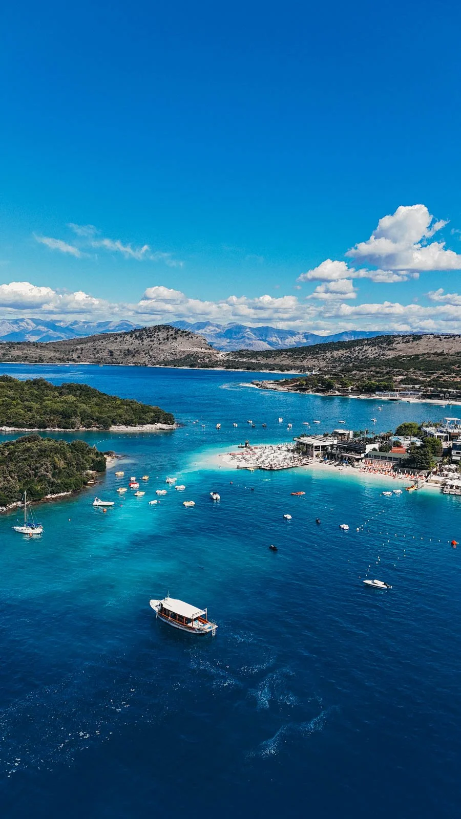 A drone photo above the a small group of small islands in Southern Albania surrounded by blue water and many boats.