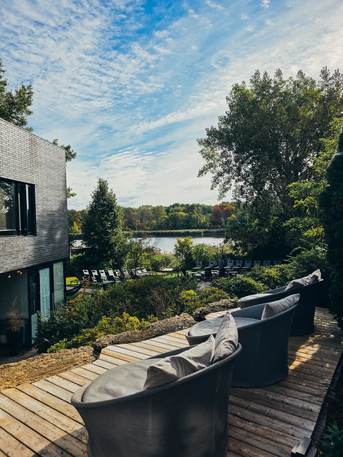 A deck area outdoors with cushioned seating and a lawn beyond with many sunloungers at Strom Spa in Montreal