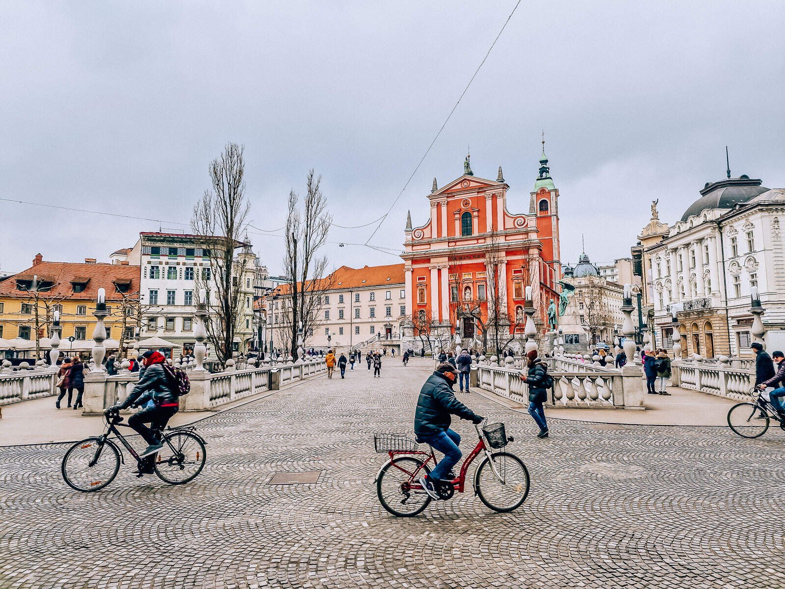 people cycling on a cobbled street in front of a pink church in ljubljana