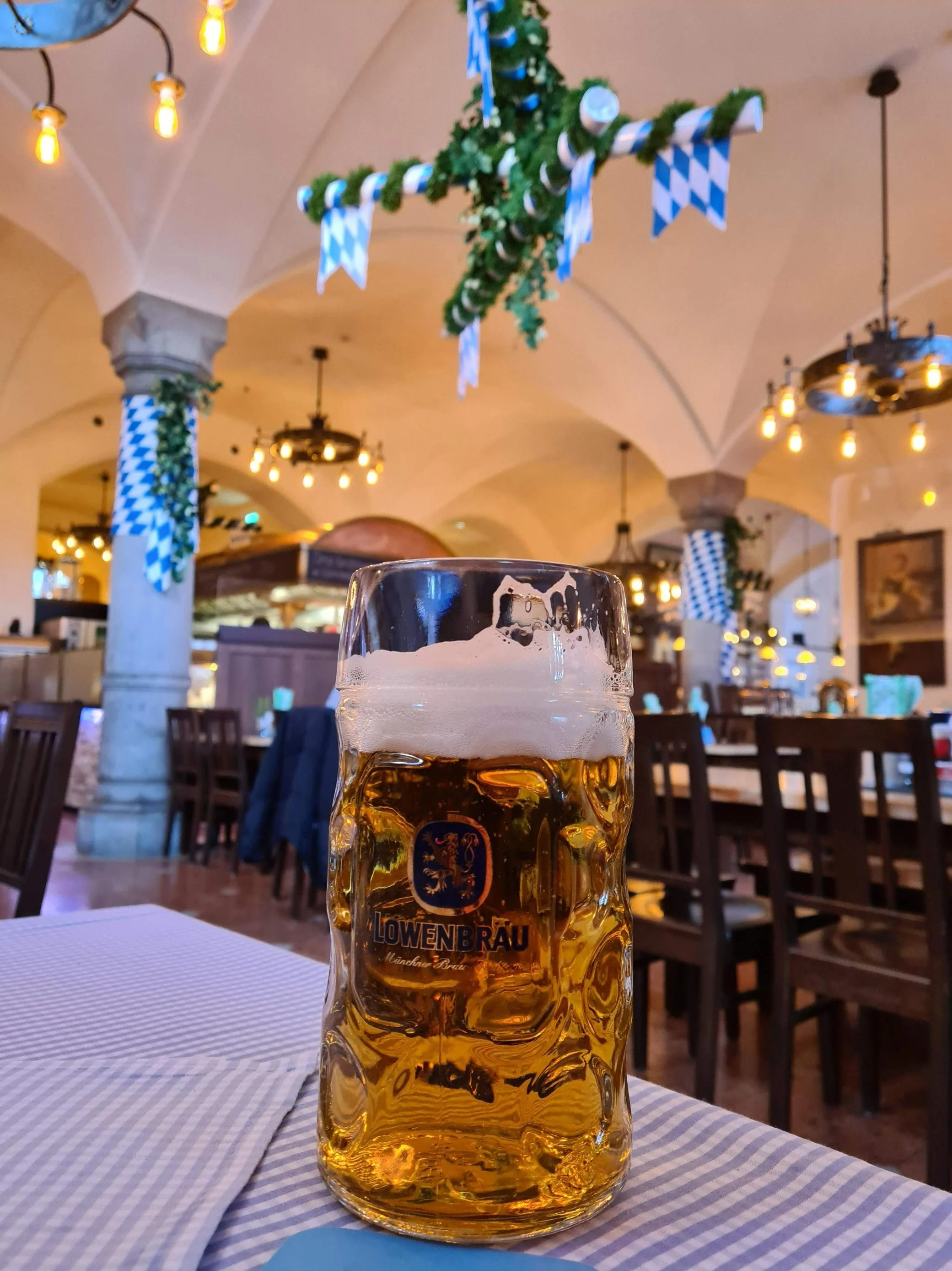 A large beer stein filled with beer on a blue checked table in a large beer hall in Munich
