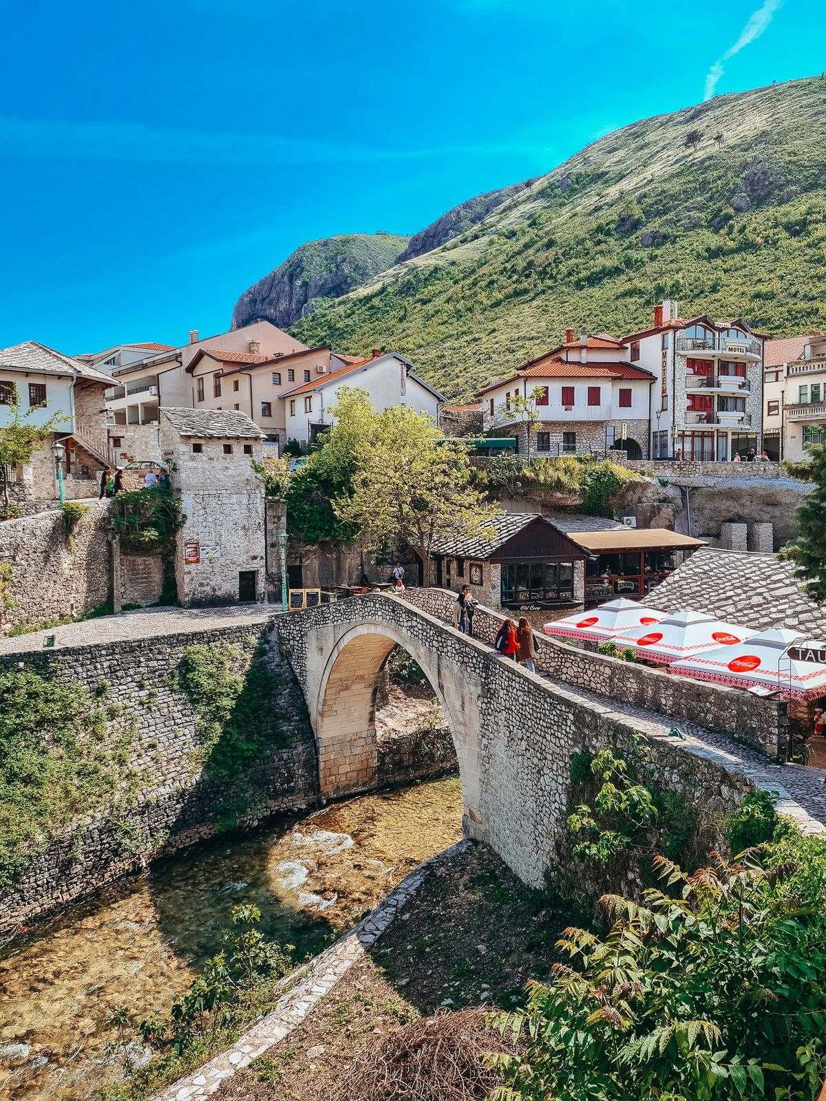a small stone bridge with houses and a mountain in the backgroun