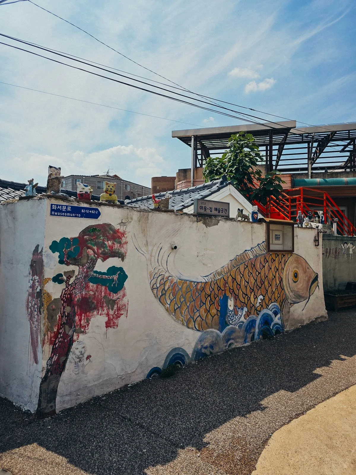 A small white wall with a mural of a fish painted on it along a small road in the middle of a village