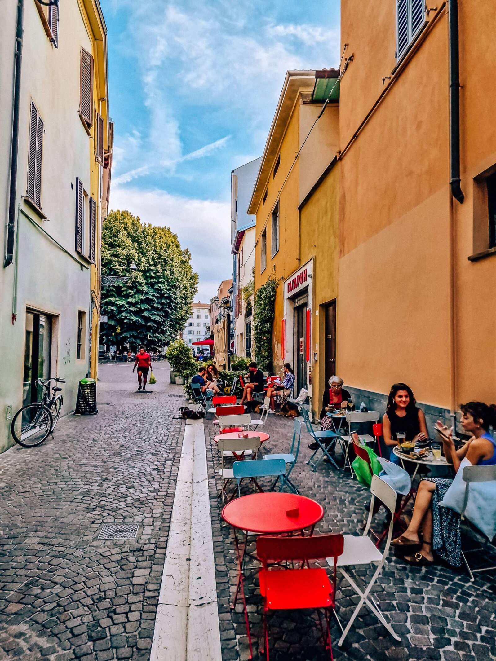 A cobblestone street with the colourful tables of a restaurant lining one side of the street