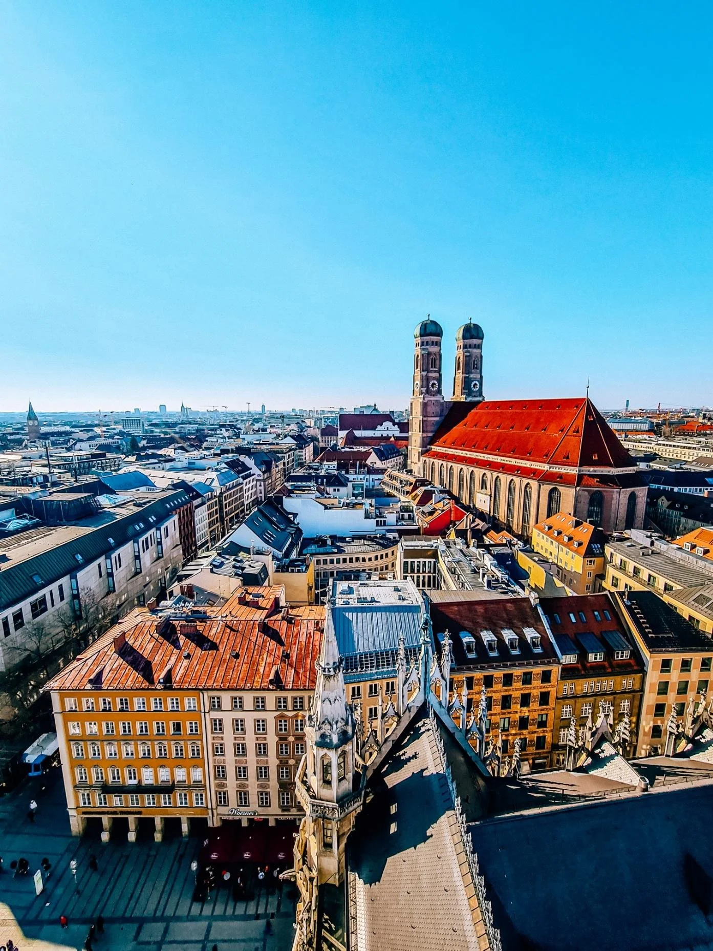 A rooftop view of Munich's old town with a large red roofed church surrounded by many colourful buildings and church spires