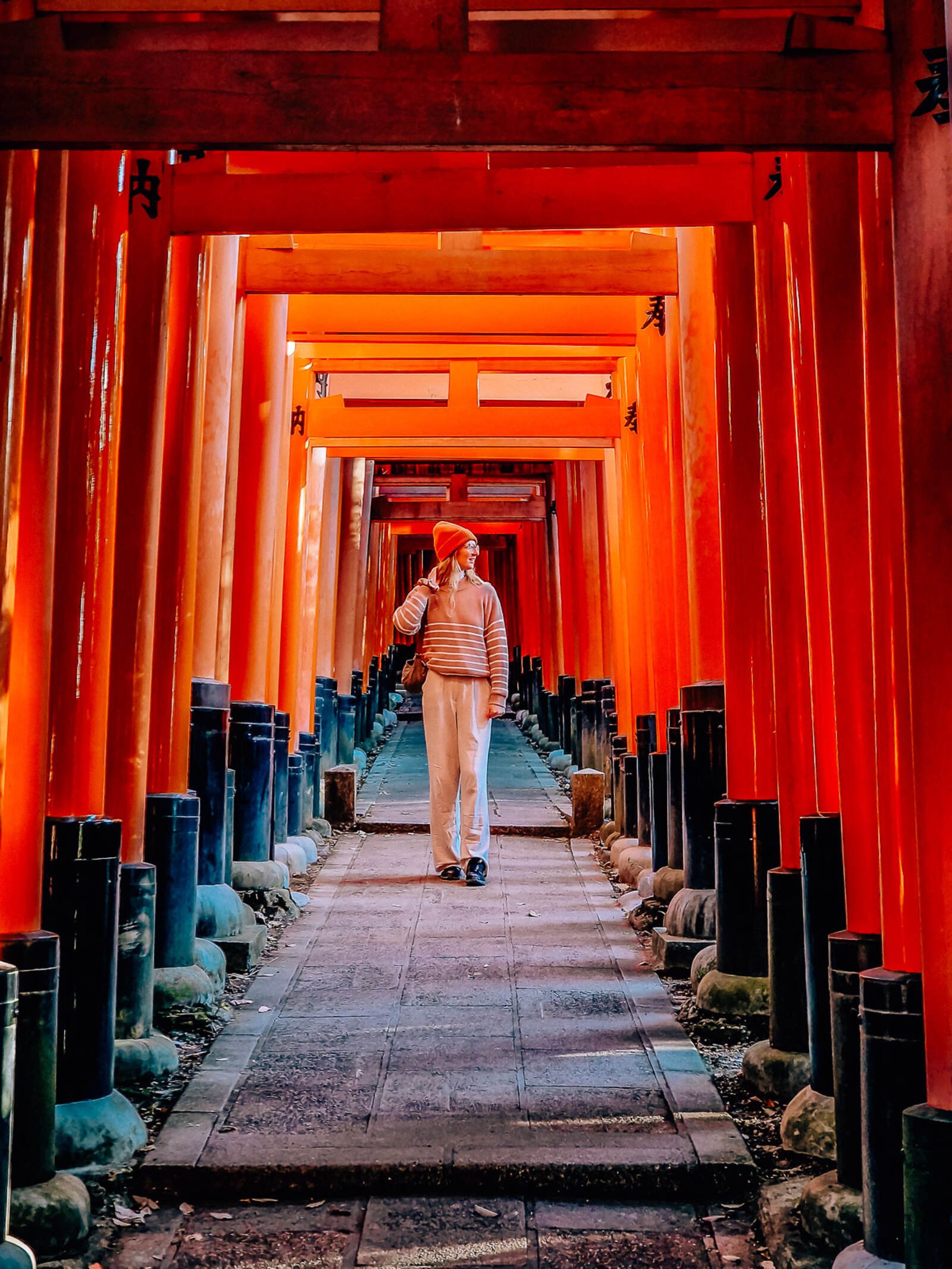 Helena walking down a paved path lined with orange torii gates in Kyoto Japan