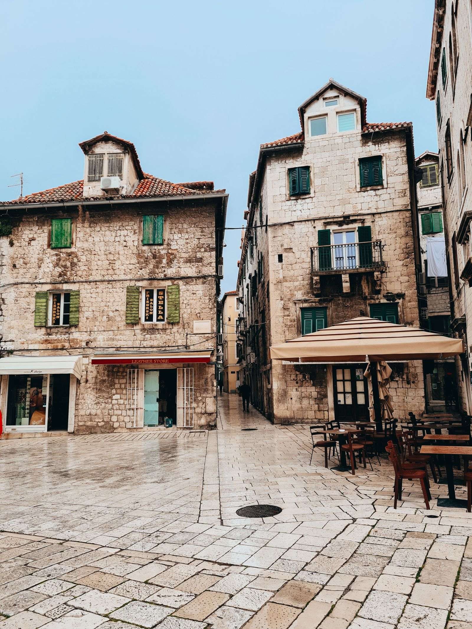 Two old stone buildings with green shutters and an alleyway between the two. The ground is cobbled. In the old town of Split, Croatia