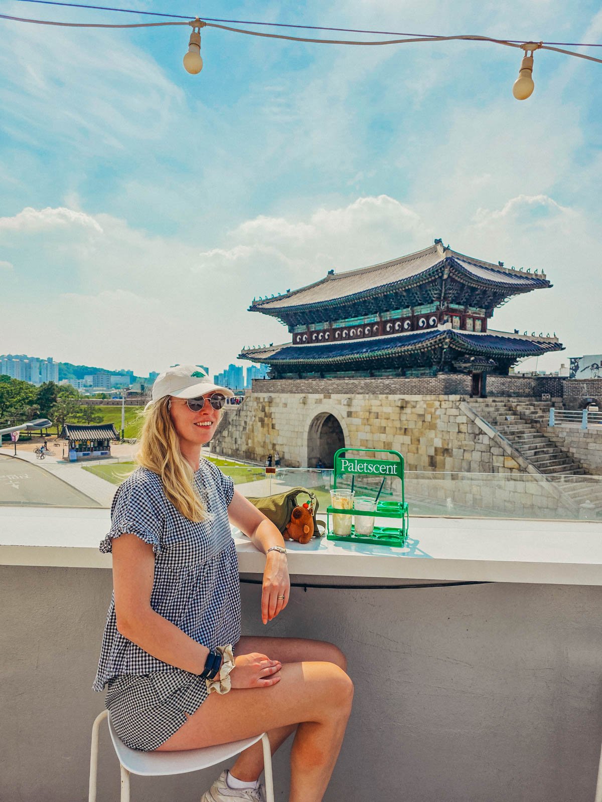 Helena sitting at a rooftop cafe with a ornate Korean fortress gate in the distance