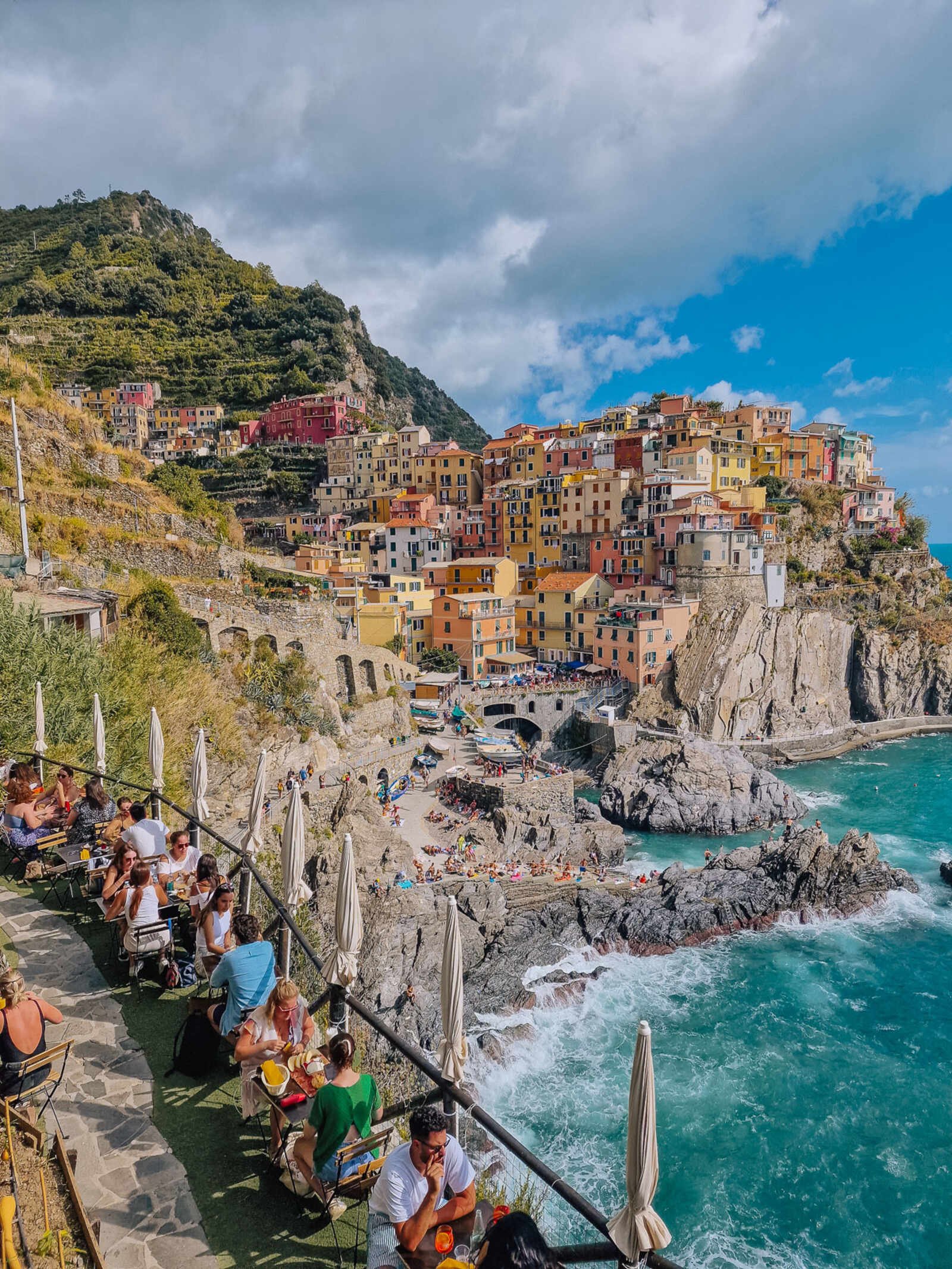 Looking down on the terrace at the famous restaurant in Manarola Cinque Terre with people sitting at lables and the view of the village behind them