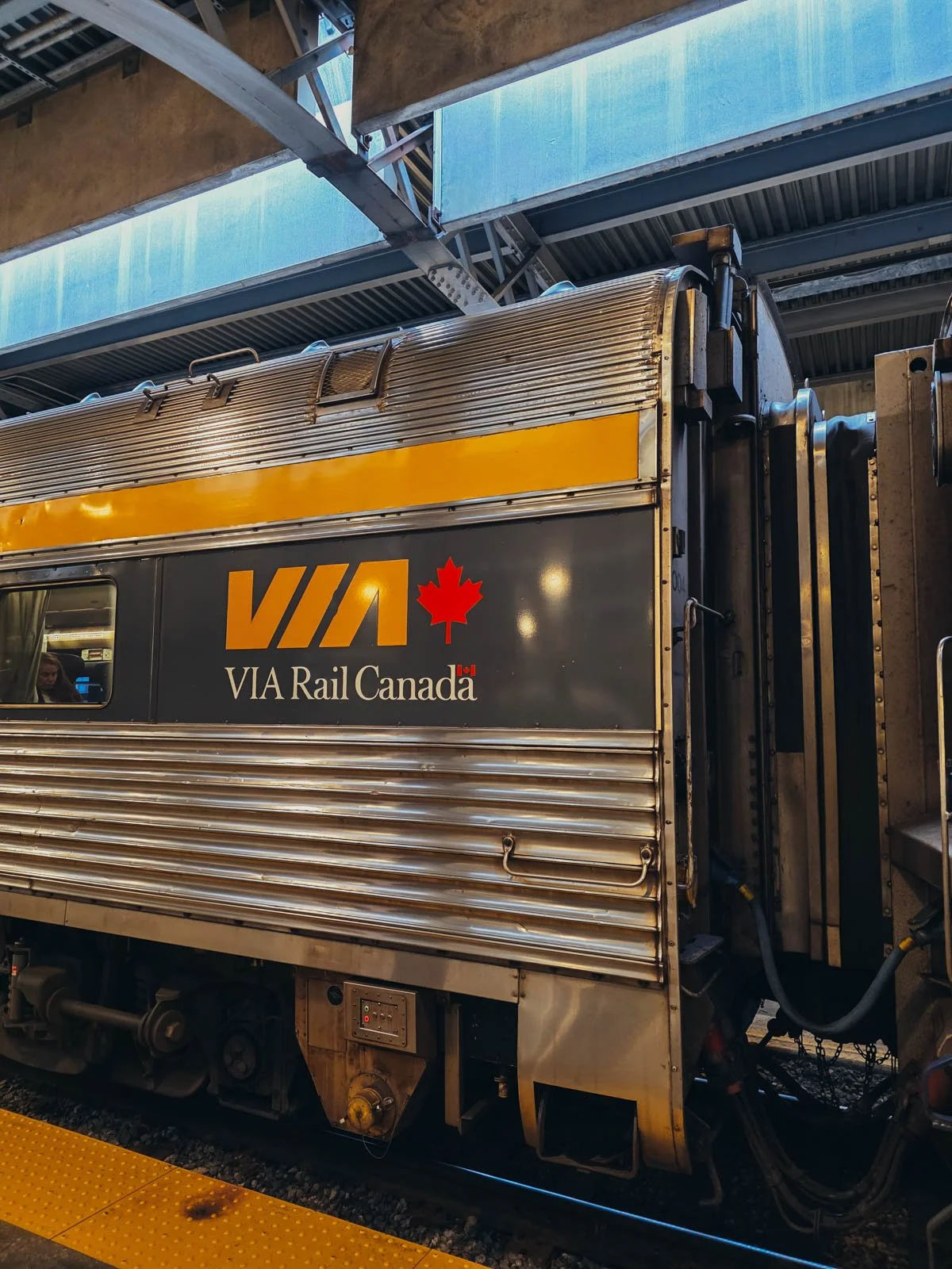 The exterior of a metal train in the station with branding on it that reads "VIA Rail Canada"