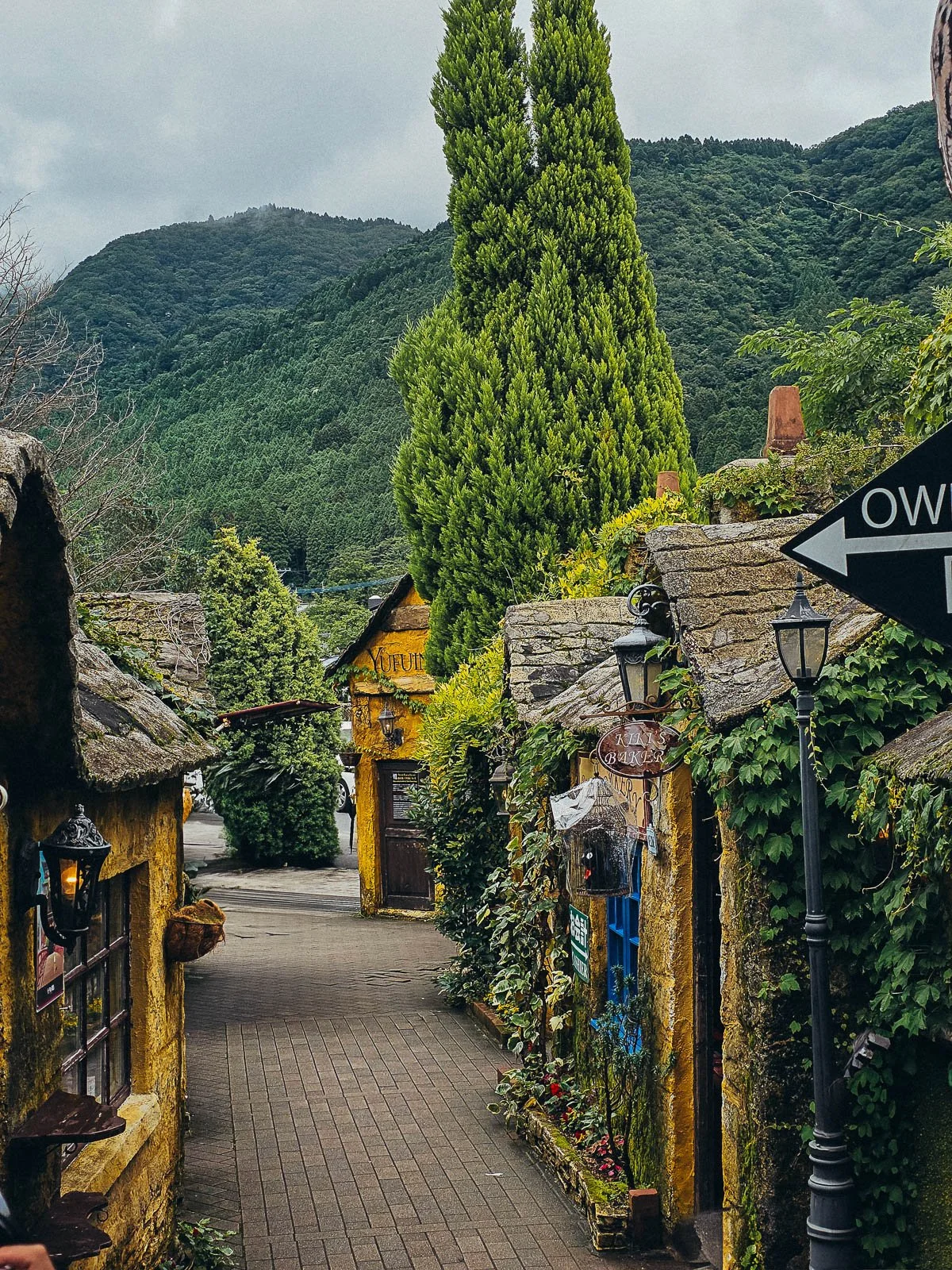 a narrow path lined with yellow cottage style houses and small black lampposts in the fairytale village of Yufuin in Kyushu Japan