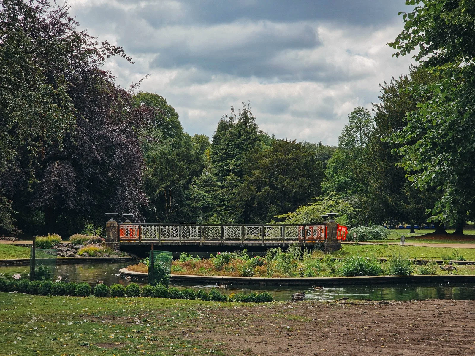 Lush green gardens with a low pedestrian bridge over a river