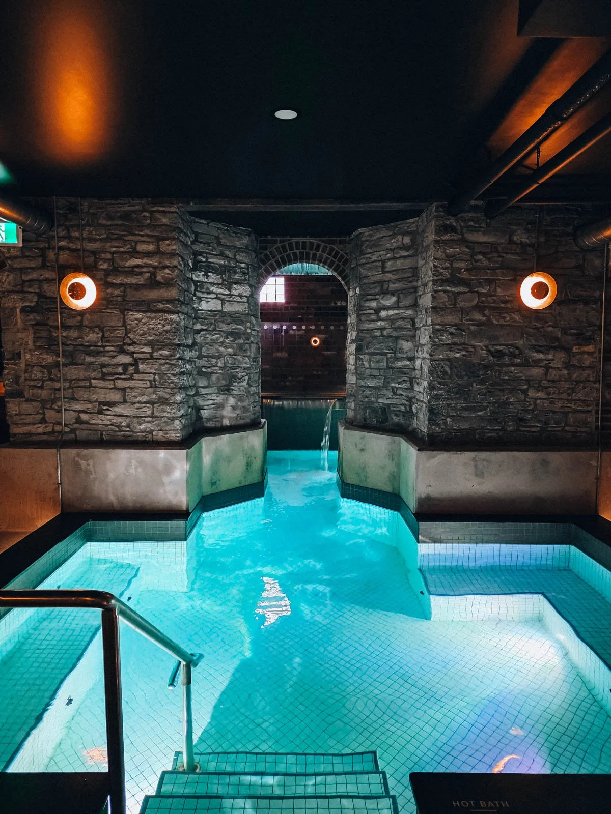 The large blue pool of a spa with stone walls which is in the the basement of a hotel
