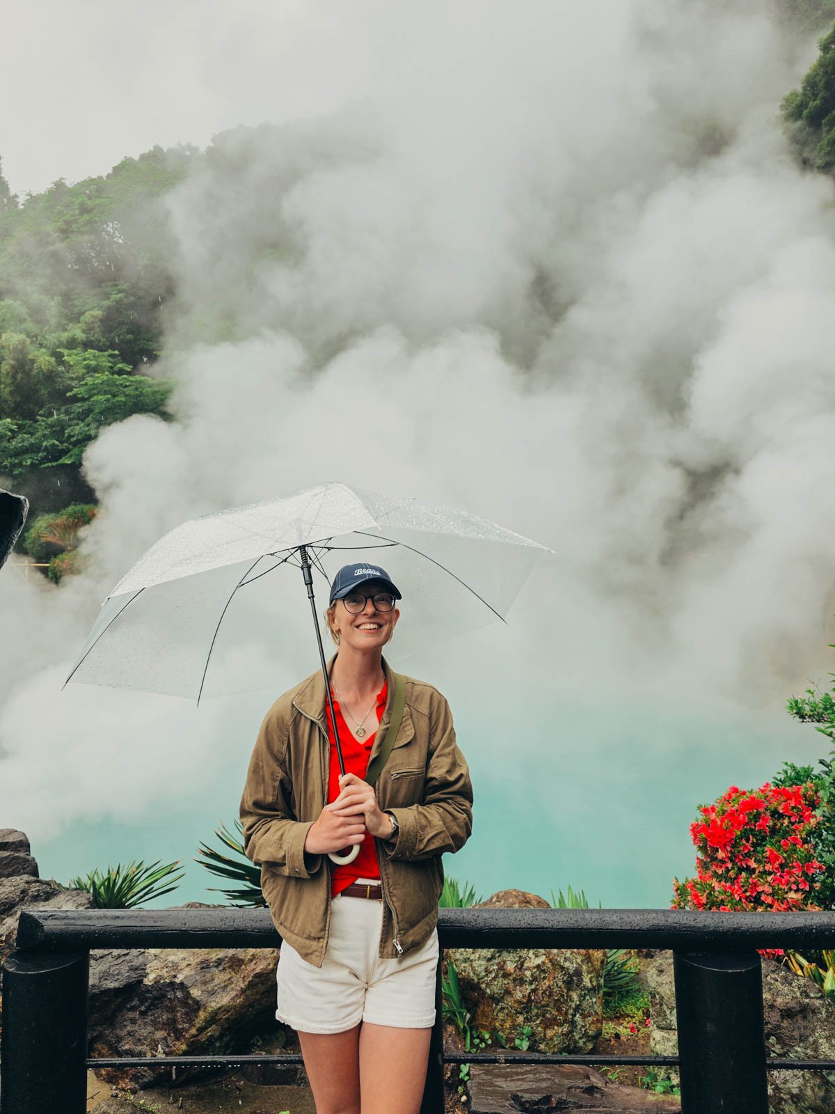 Helena standing with an umbrella in front of a blue pool of steam at the Hells of Beppu