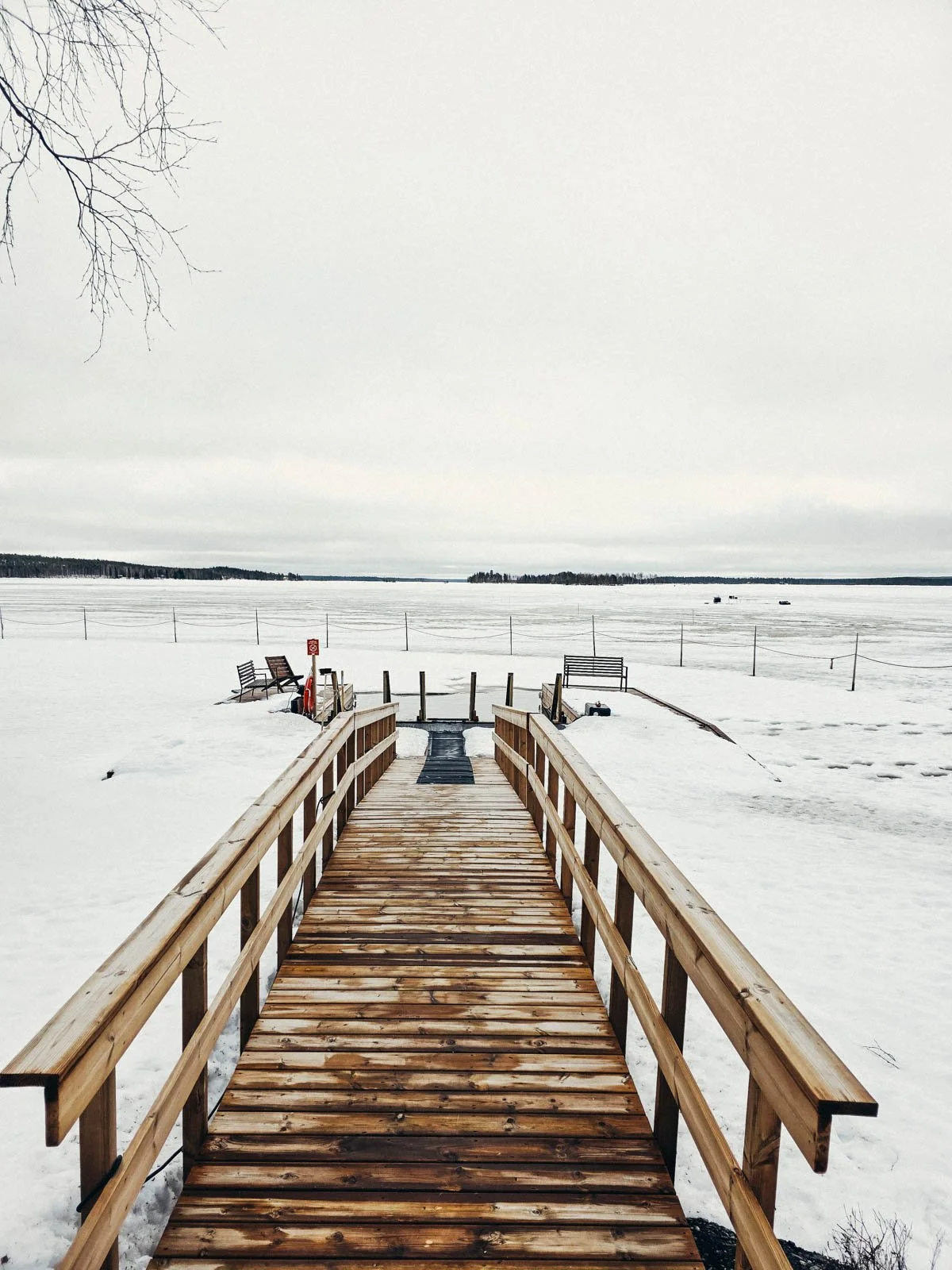 A wooden bridge leading to a hole in a frozen lake used for cold plunging. The lake is also used for ice fishing activities in Rovaniemi