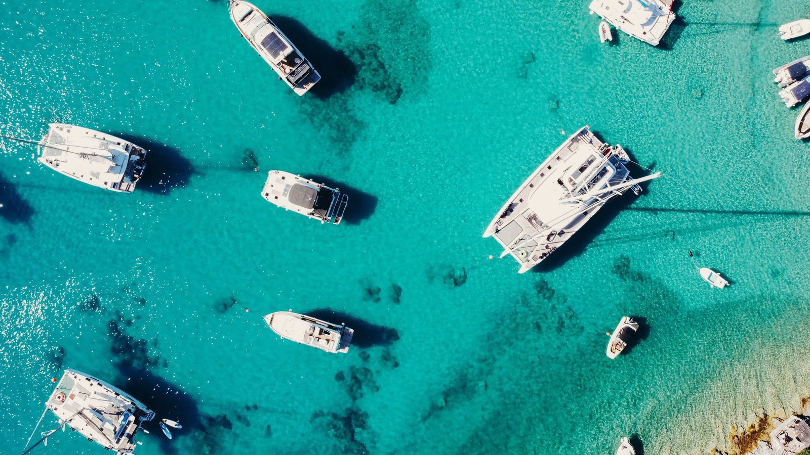 top down drone shot if turquoise sea and many white sailing ships anchored