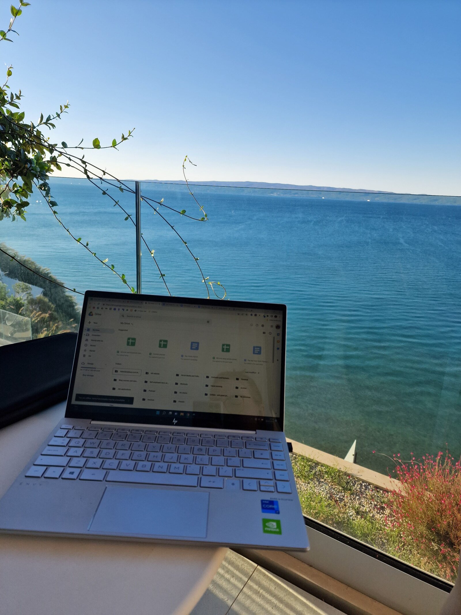 A laptop on a table looking out of a balcony with blue sea and blue sky right there
