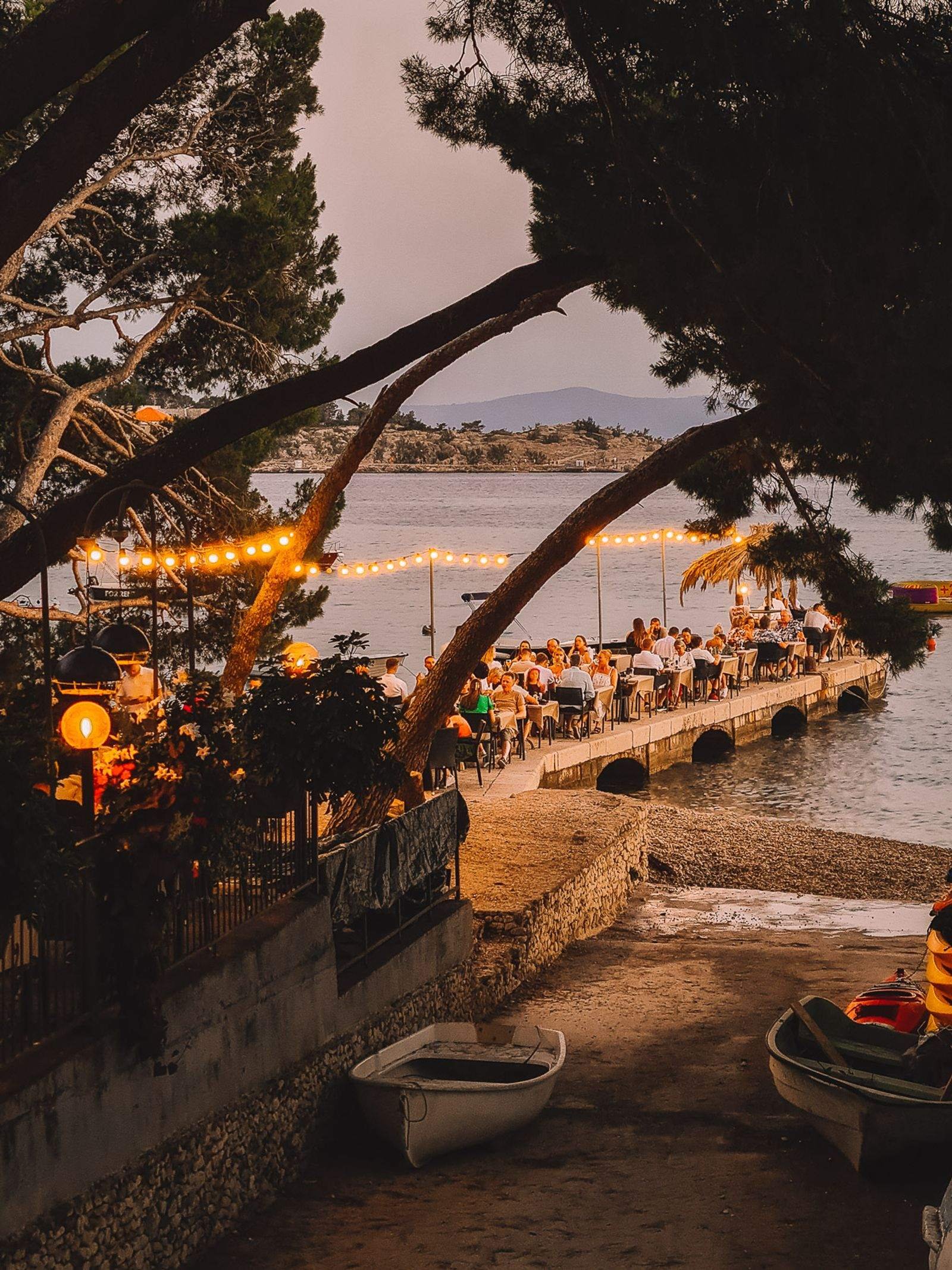 restaurant seating along a pier with fairy lights strung in the trees at dusk