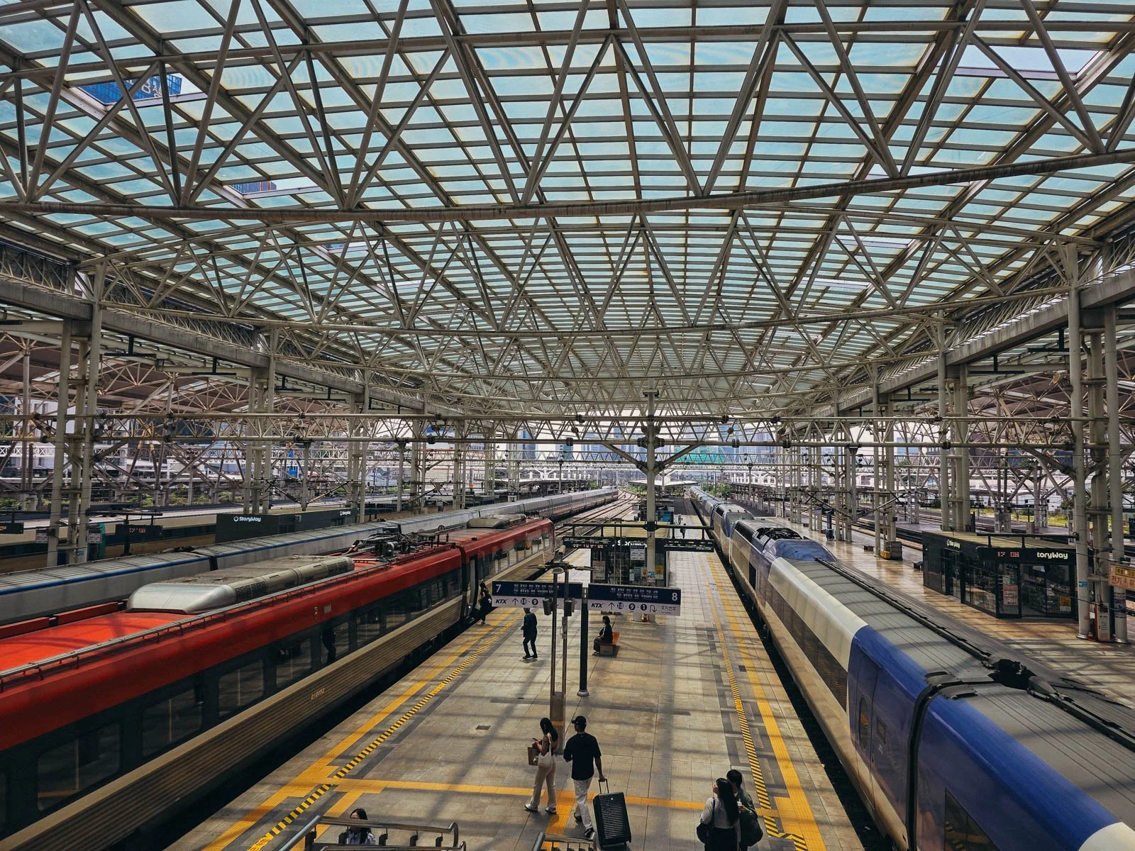 A large train station with one red train and one blue train stopped along the train station platform