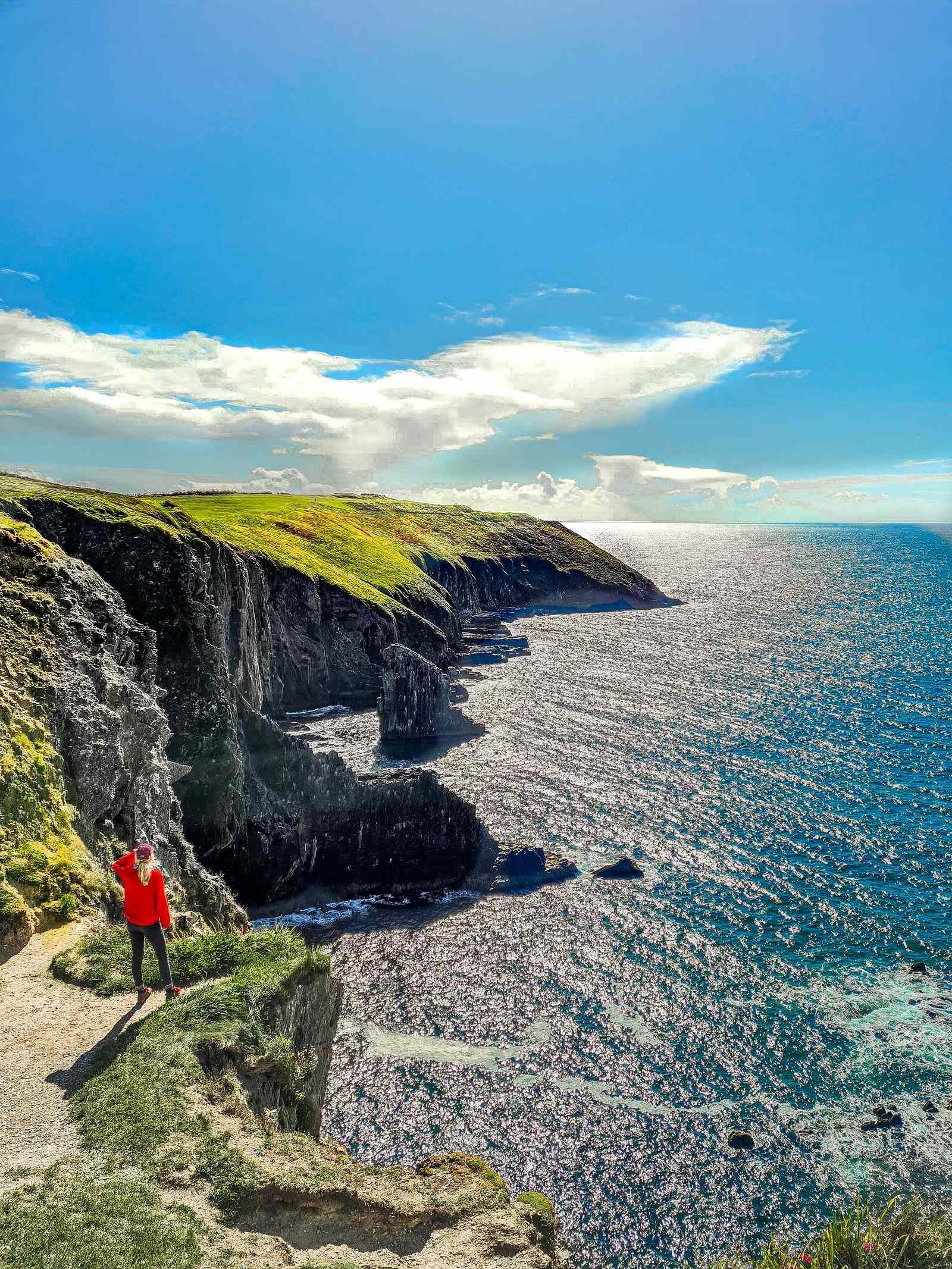 Girl in red on the edge of a cliff looking out onto the steep rocky shore and blue ocean