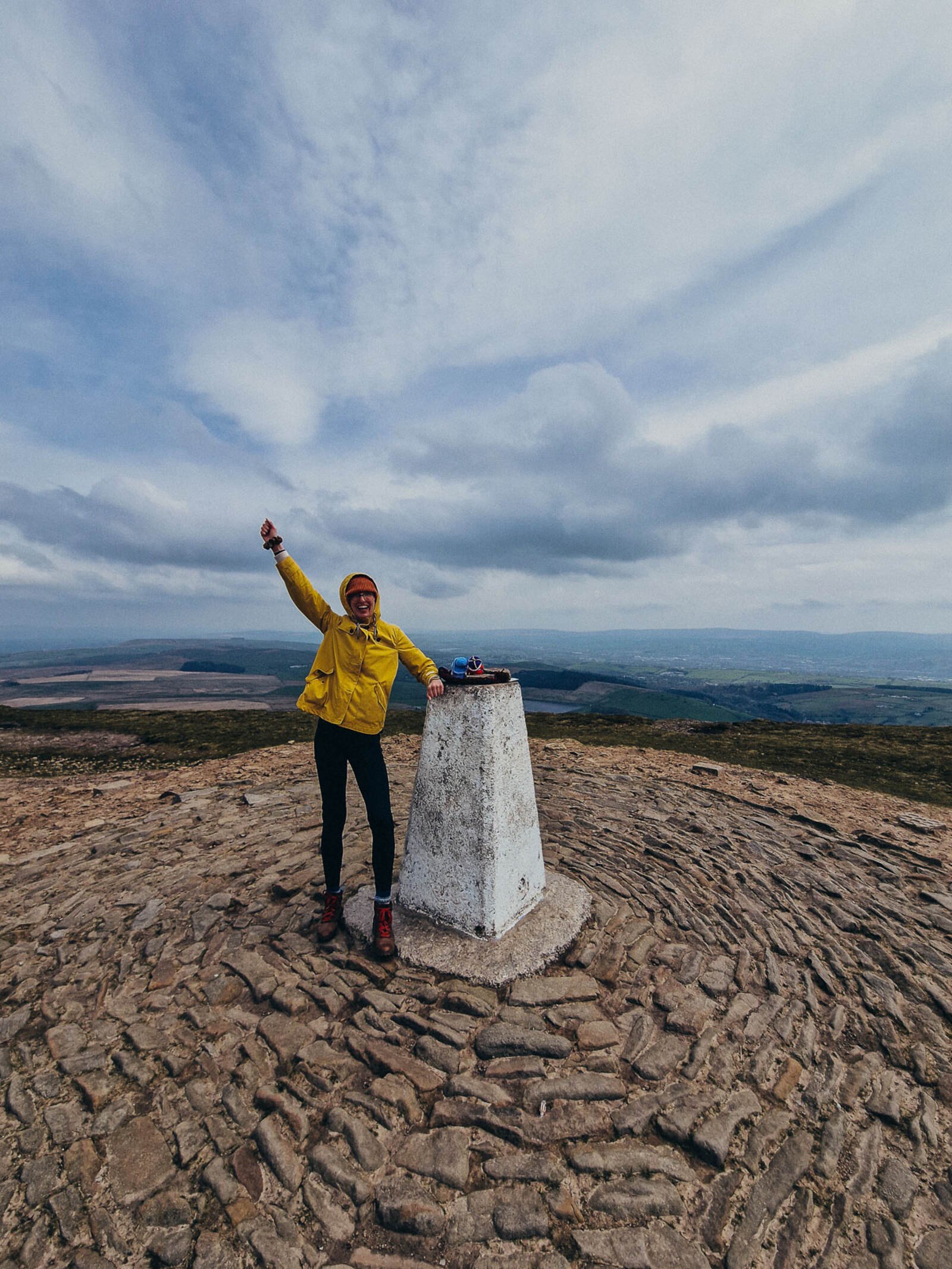 woman in a yellow coat celebrating reaching the peak of Pendle Hill