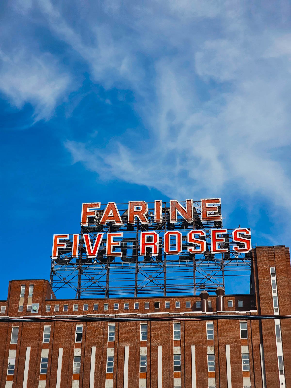 The top of a brick building with an old-style red sign on the top that reads "Farine Fave Roses"