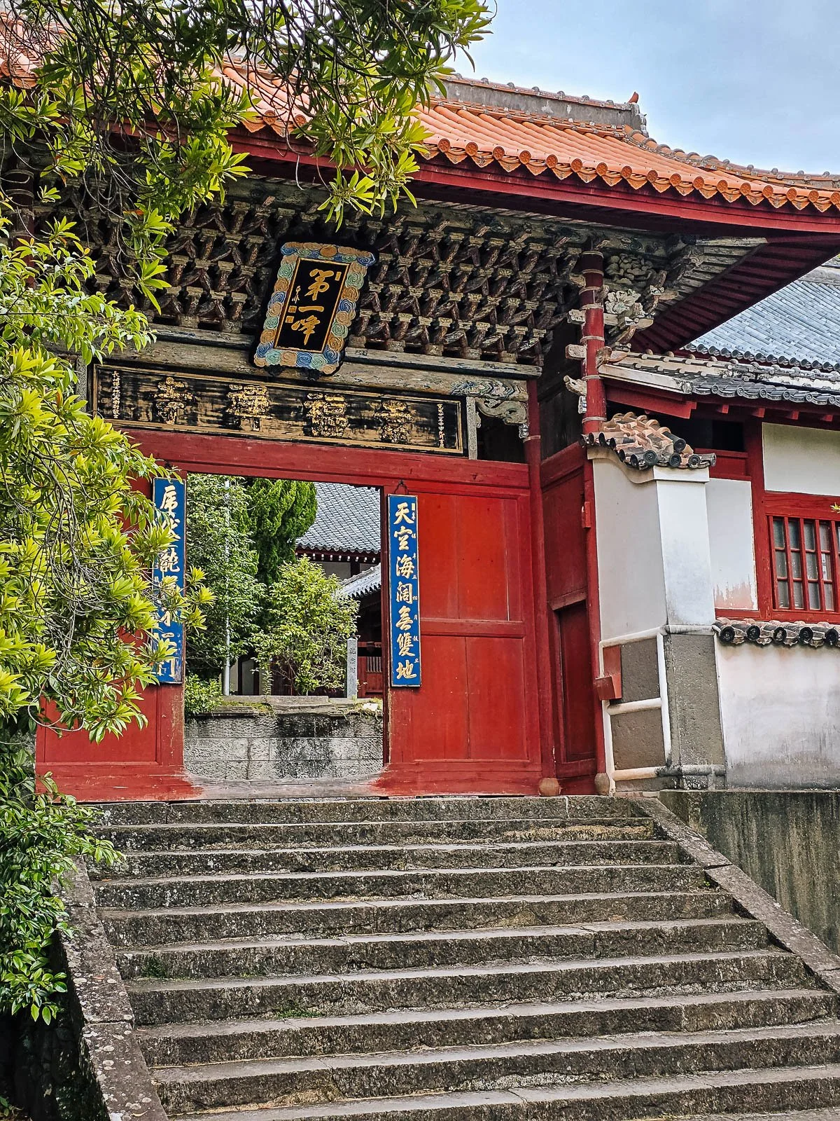 An old wooden temple gate with doors painted red and stone steps leading up to it