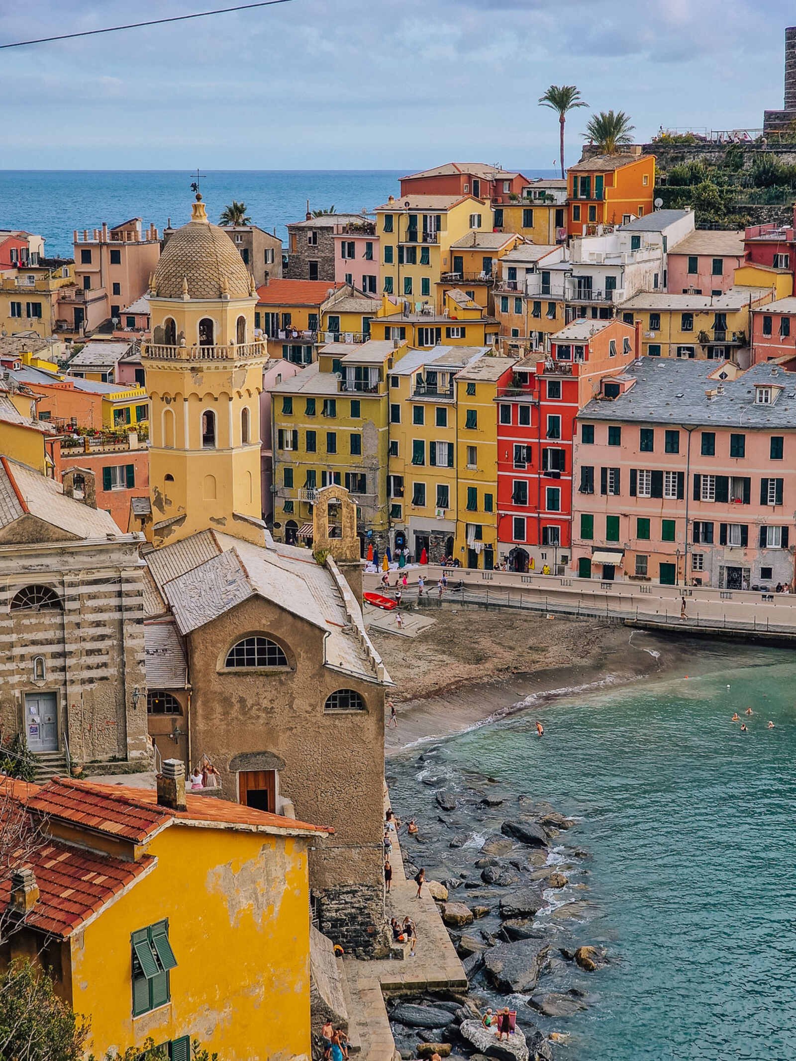 a yellow church tower with the buildings of vernazza behind