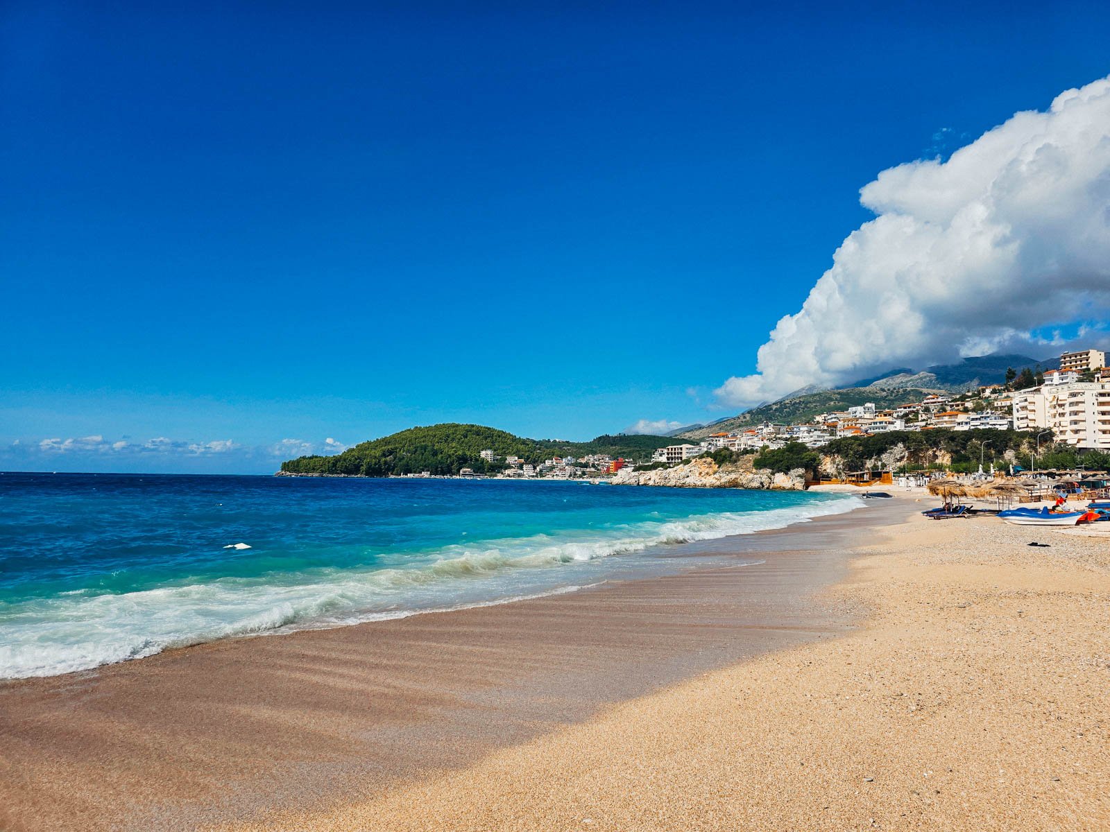 A sandy beach in Himare with clear blue water. Many hills are on green hills in the background