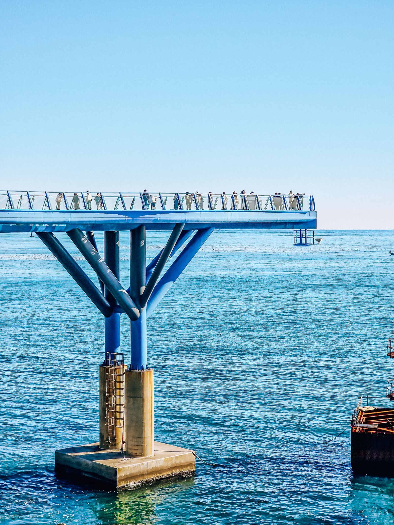 a large blue observatory deck in the water with people standing on it, looking out to sea