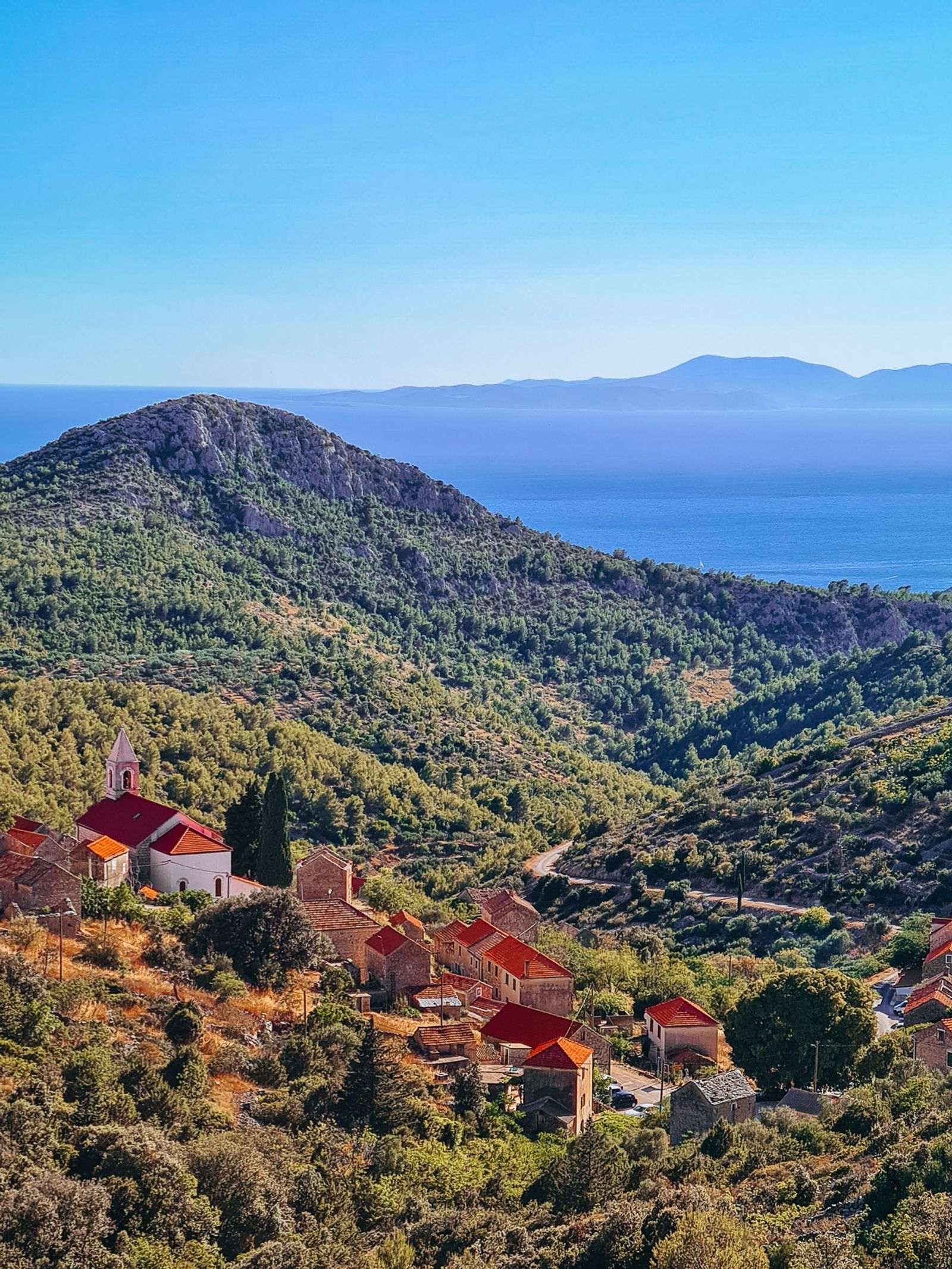 Views of green rolling hills from the top of a mountain in Hvar island. Blue sea in the distance and orange roofed houses in the valley below