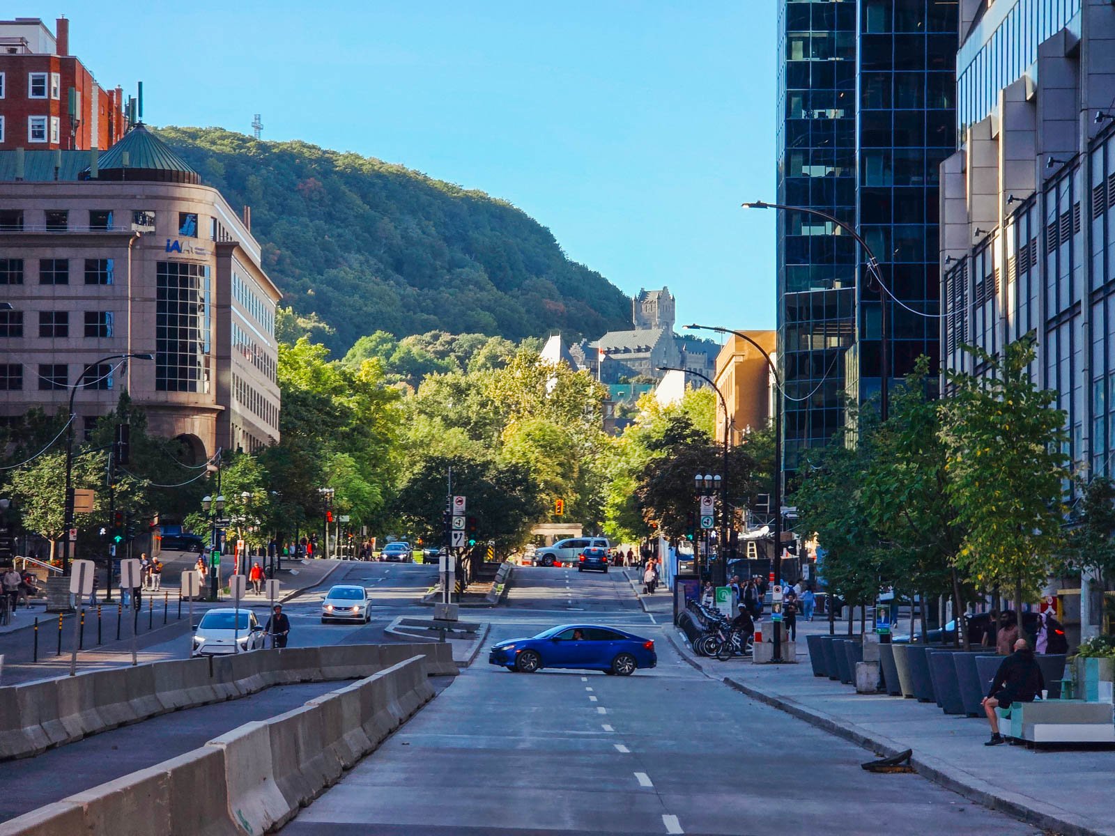 Looking up a main road in downtown Montreal towards the tree covered hill of Mont Royal in the distance