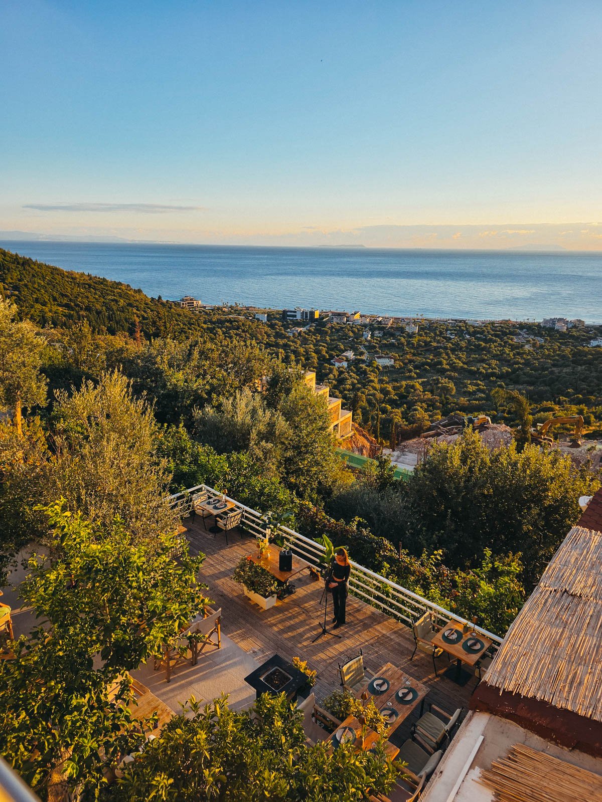 The coastal view of the Albanian Riviera  from a hotel balcony with blue water and green trees stretched out into the distance during sunset from a hotel in Himare