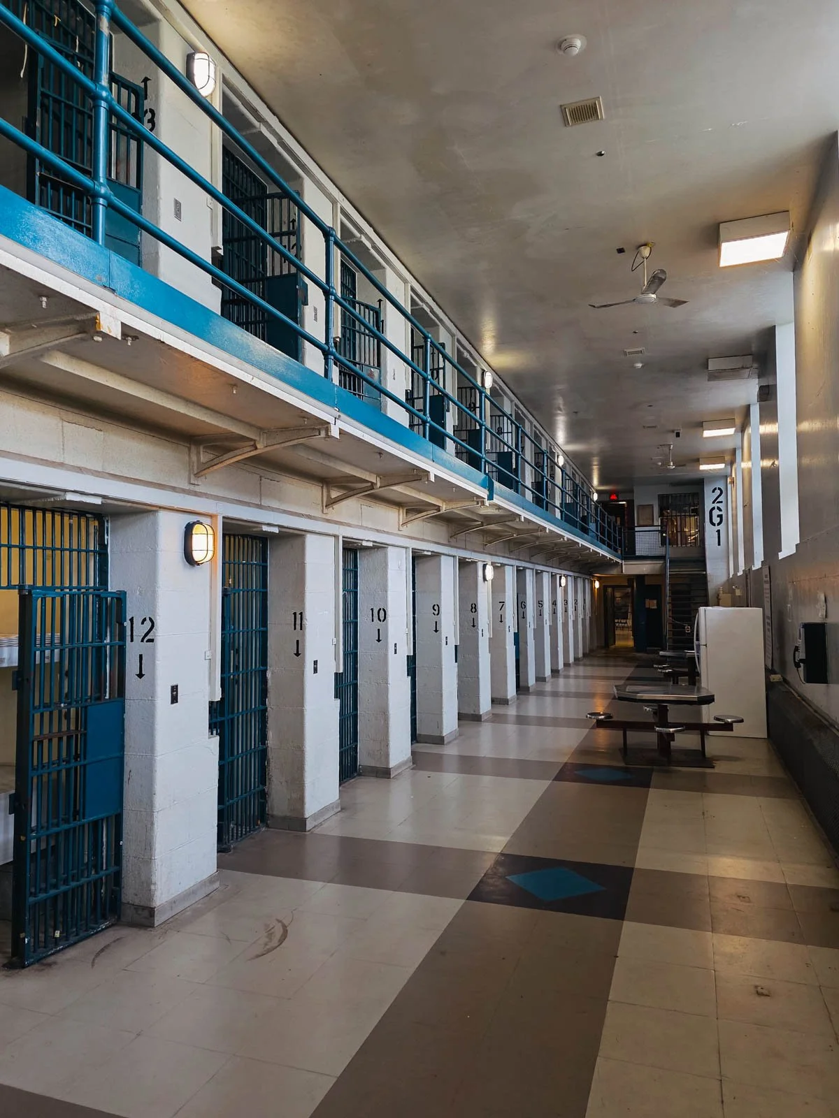 Many blue barred prison cells along a long cell block of a prison