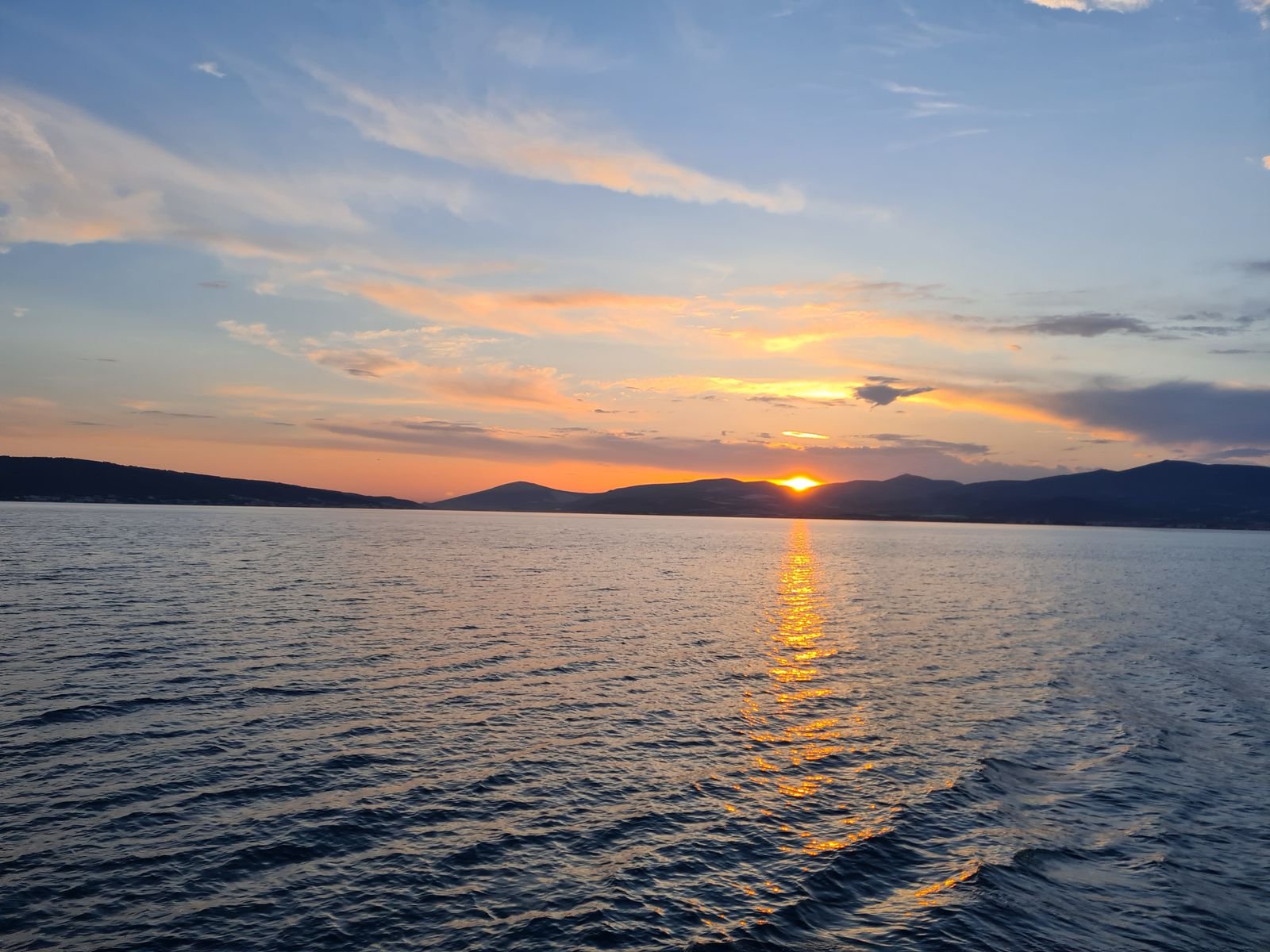 the sun disappearing behind mountains in the distance, taken from the water on a boat on the sea