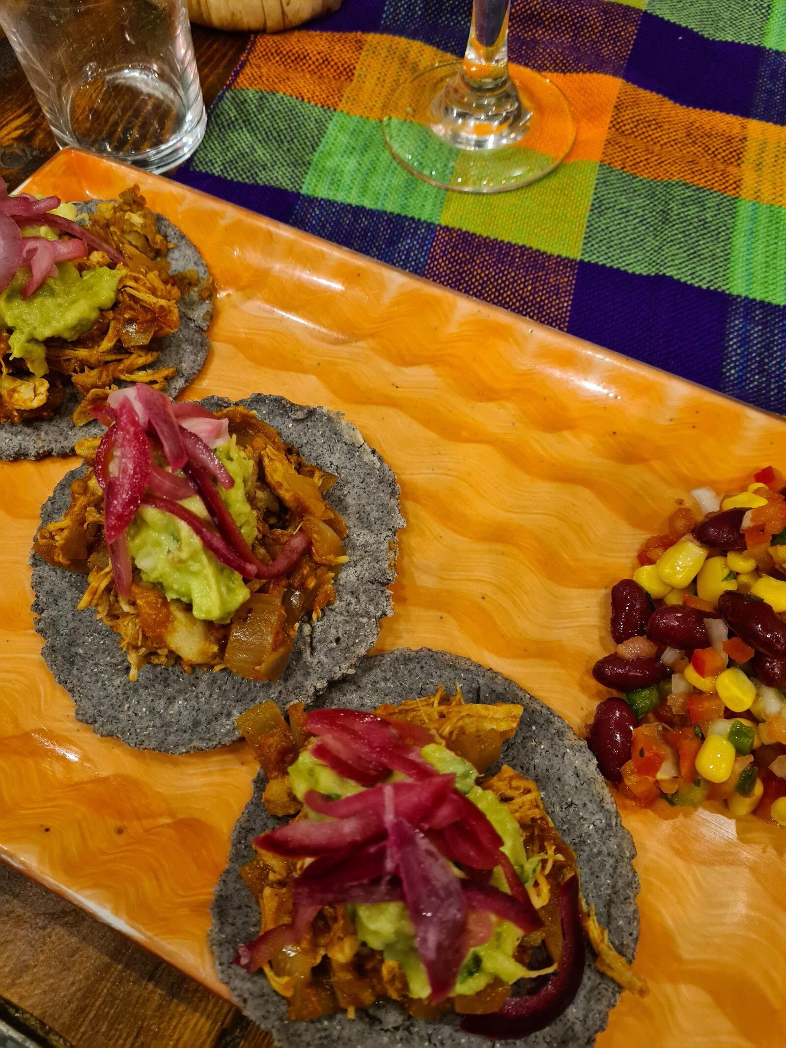 A orange plate with three small grey tacos topped with  many colourful ingredients