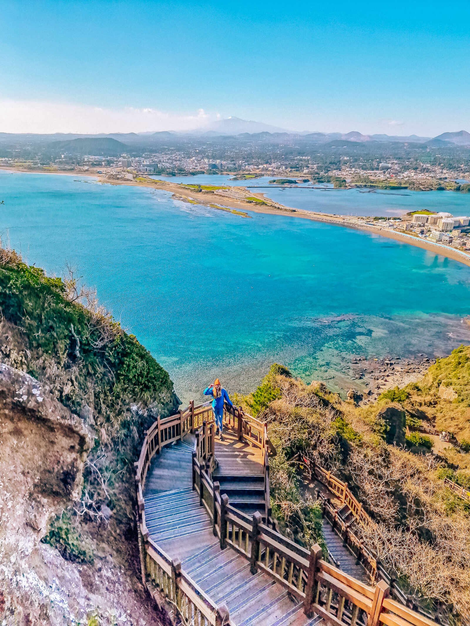 a wooden curving staircase on a cliff overlooking a turquoise blue bay
